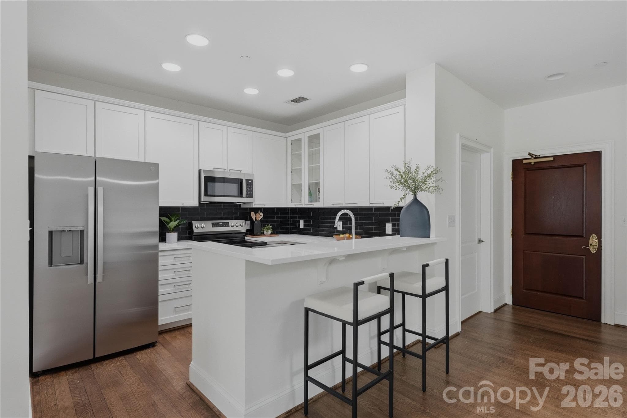 A chef's dream kitchen featuring white shaker cabinets to the ceiling, stainless steel appliances, dramatic black subway tile backsplash, and a spacious peninsula all visible the moment you walk through the door. - Charlotte