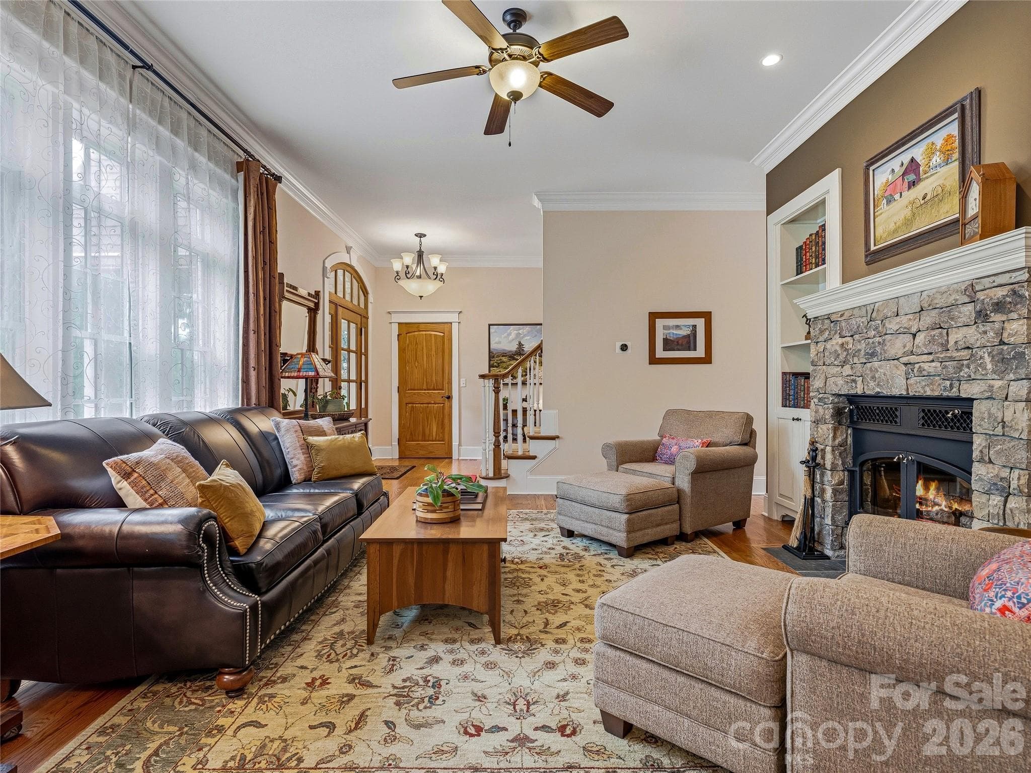 Bright and Inviting Living Room with Stone Fireplace, Hardwood Floors, Crown Moulding, and Abundant Natural Light. - Asheville