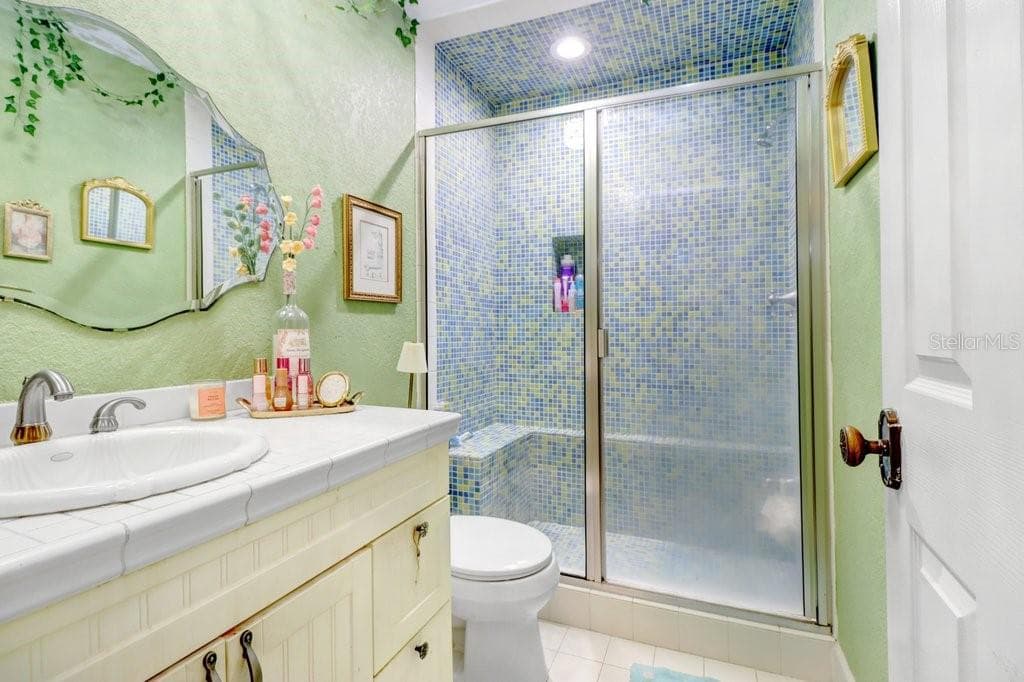 Fun upstairs full bathroom with floor to ceiling mosaic tiled shower which includes seat and shampoo nook. - 1976 DUNLOE CIR, DUNEDIN