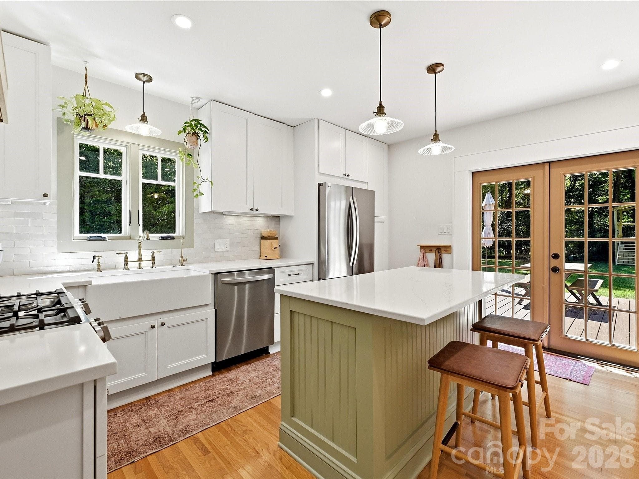 The beautifully updated kitchen features quartz countertops, a farmhouse sink, stainless steel appliances, a center island with seating, and direct access to the outdoor living space. - 3514 Kelly Road, Charlotte