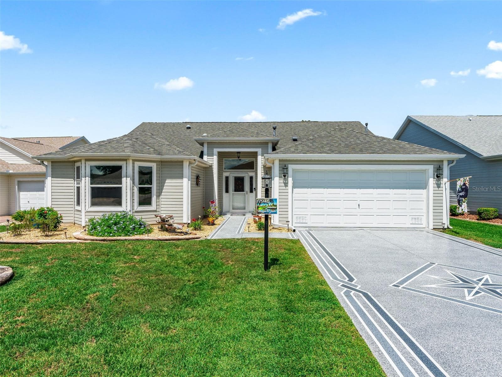 Bright and welcoming exterior featuring a neatly landscaped lawn, covered front entry, and spacious, custom painted driveway leading to the two-car garage. - 17946 SE 87TH MELROSE CT, THE VILLAGES