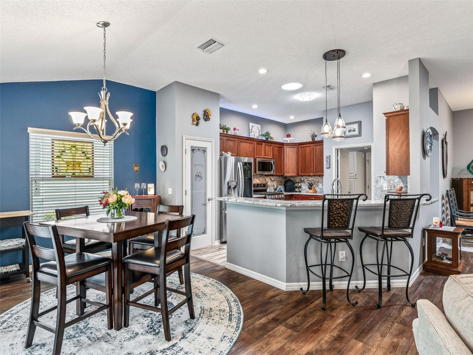 The open layout connects the dining area and kitchen, with coordinated lighting, wood-look flooring, and a breakfast bar ideal for casual seating. - 17946 SE 87TH MELROSE CT, THE VILLAGES