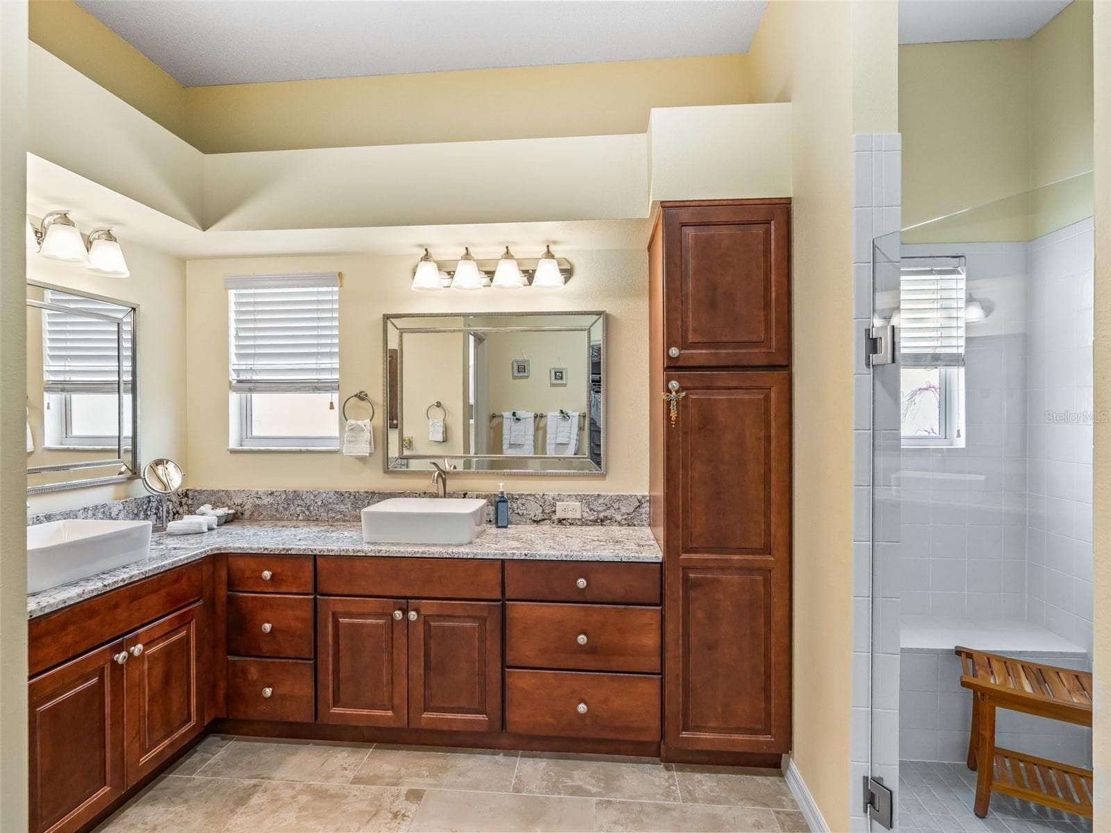 The primary bathroom offers extensive wood cabinetry, a tall linen cabinet, dual vanity areas, and multiple windows for natural light. - 17946 SE 87TH MELROSE CT, THE VILLAGES