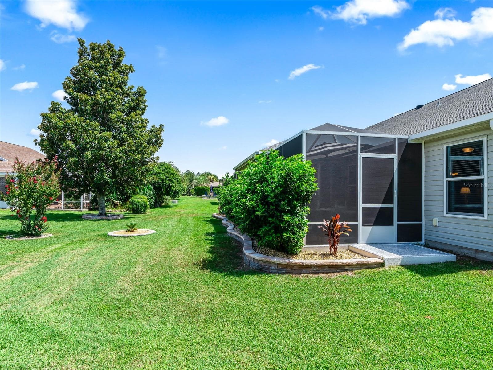 A wide lawn, mature shade tree, and environment with an open, uncrowded feelscreened lanai create a peaceful backyard - 17946 SE 87TH MELROSE CT, THE VILLAGES