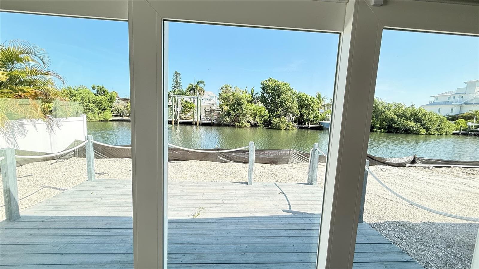 View through sliding door of deck and canal. Black tarp at seawall is for adjacent unit new pool install. - 420 63RD ST #420A, HOLMES BEACH