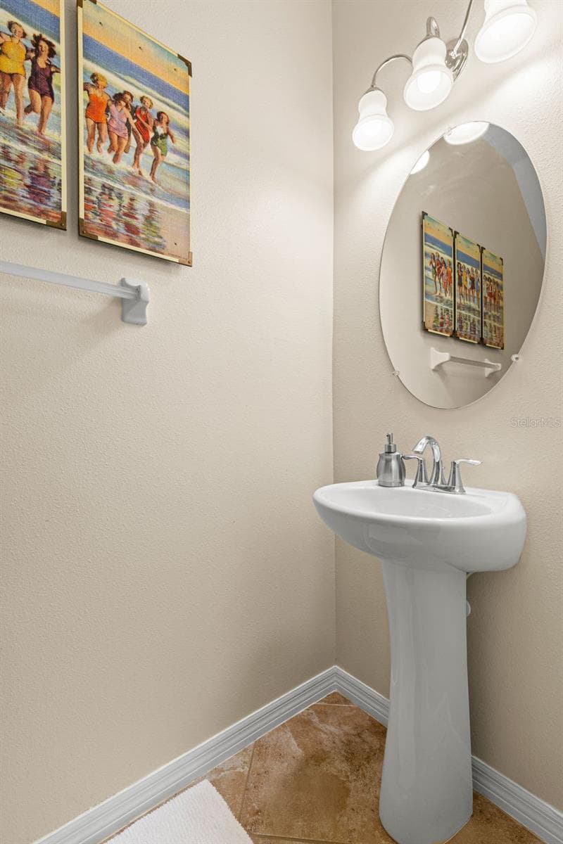 The first-floor powder room features a pedestal sink, oval mirror, down light fixture and neutral tile flooring. - 9524 TRUMPET VINE LOOP, NEW PORT RICHEY