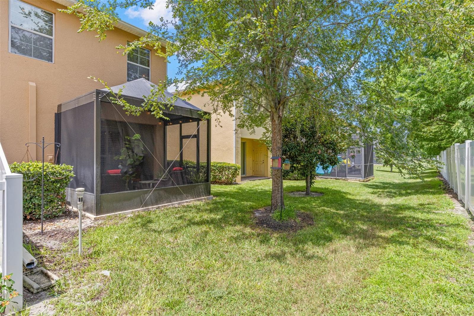 The rear common area is lined with mature trees and a vinyl fence, creating a green, shaded backdrop behind the screened lanai. - 9524 TRUMPET VINE LOOP, NEW PORT RICHEY