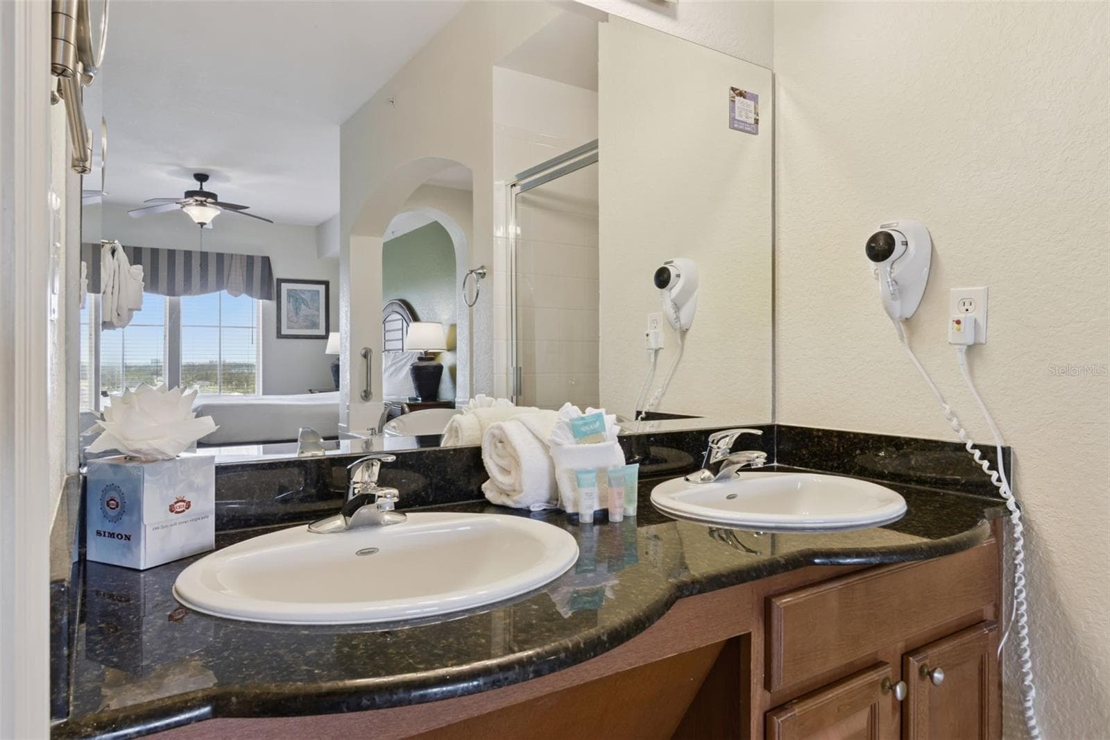 Bathroom Vanity | A granite-top vanity with dual sinks, wood cabinetry, and a large mirror offers useful storage. - 8101 RESORT VILLAGE DR #31110, ORLANDO