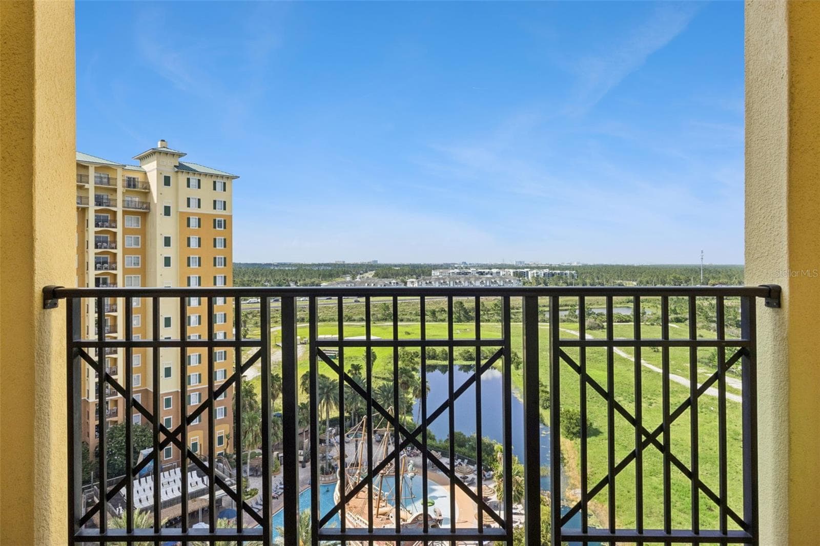 Balcony Outlook | Open railing preserves sweeping views of the pool area, neighboring tower, pond, and surrounding landscape. - 8101 RESORT VILLAGE DR #31110, ORLANDO