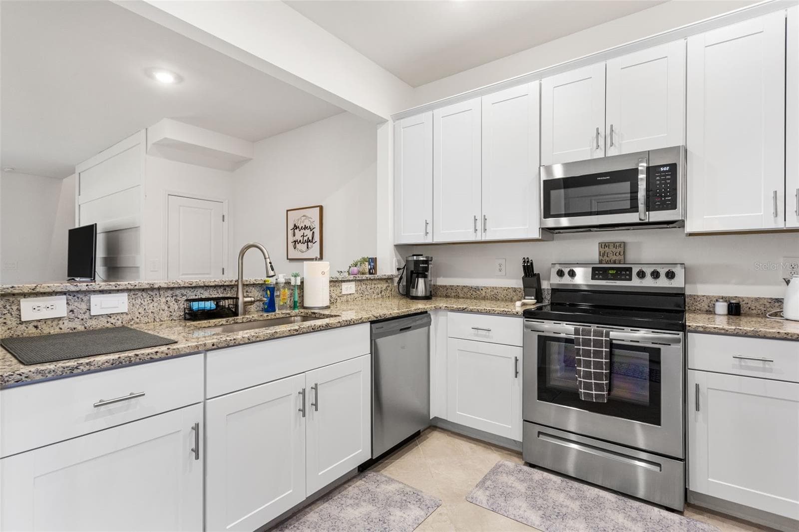 Bright, spacious kitchen featuring white shaker cabinetry, granite countertops, and stainless steel appliances - 14275 PINE LODGE LN, FORT MYERS