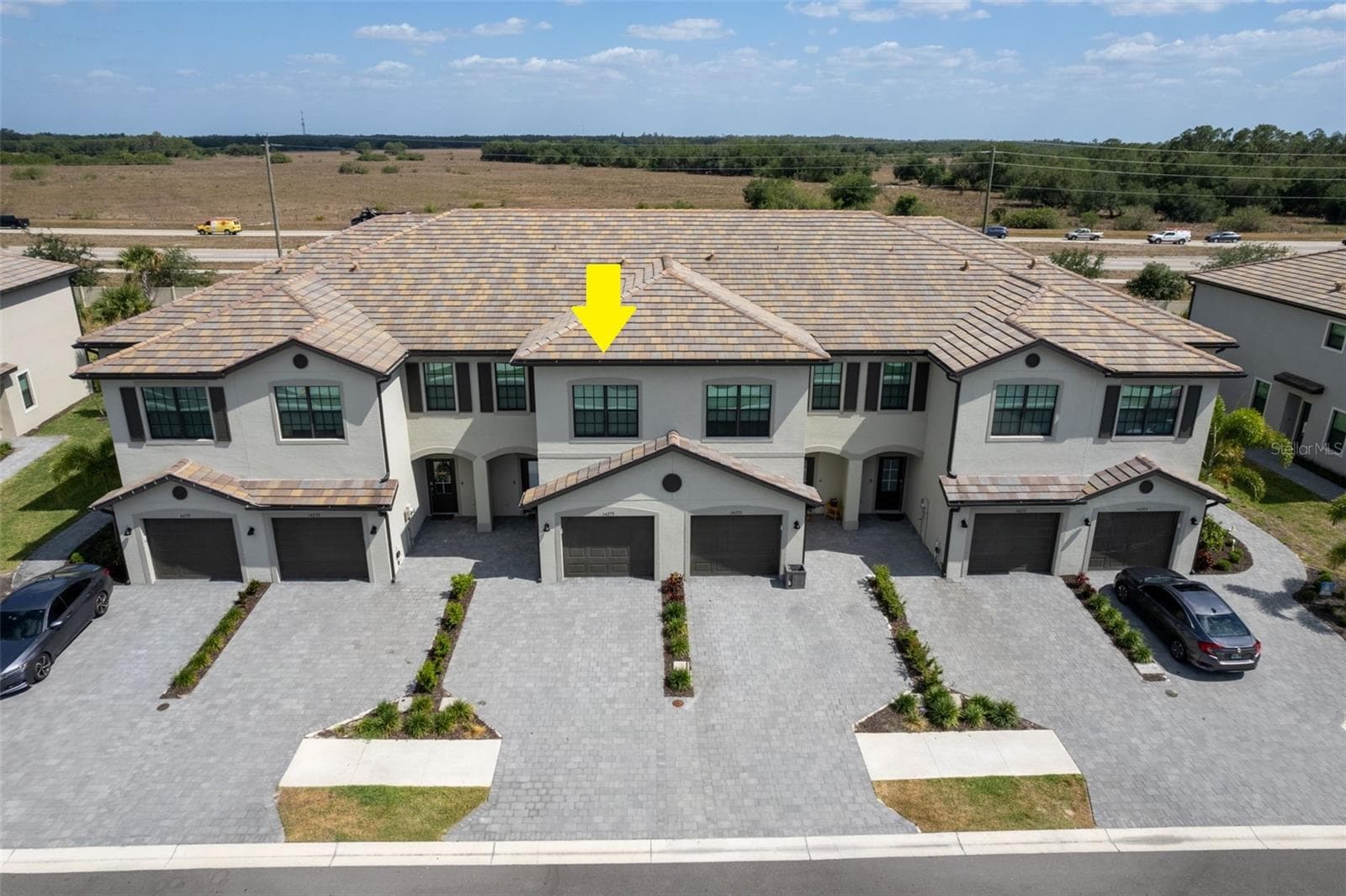 Aerial view highlighting the townhome’s attractive exterior, attached one-car garage, driveway parking for an additional vehicle, plus convenient guest parking nearby - 14275 PINE LODGE LN, FORT MYERS
