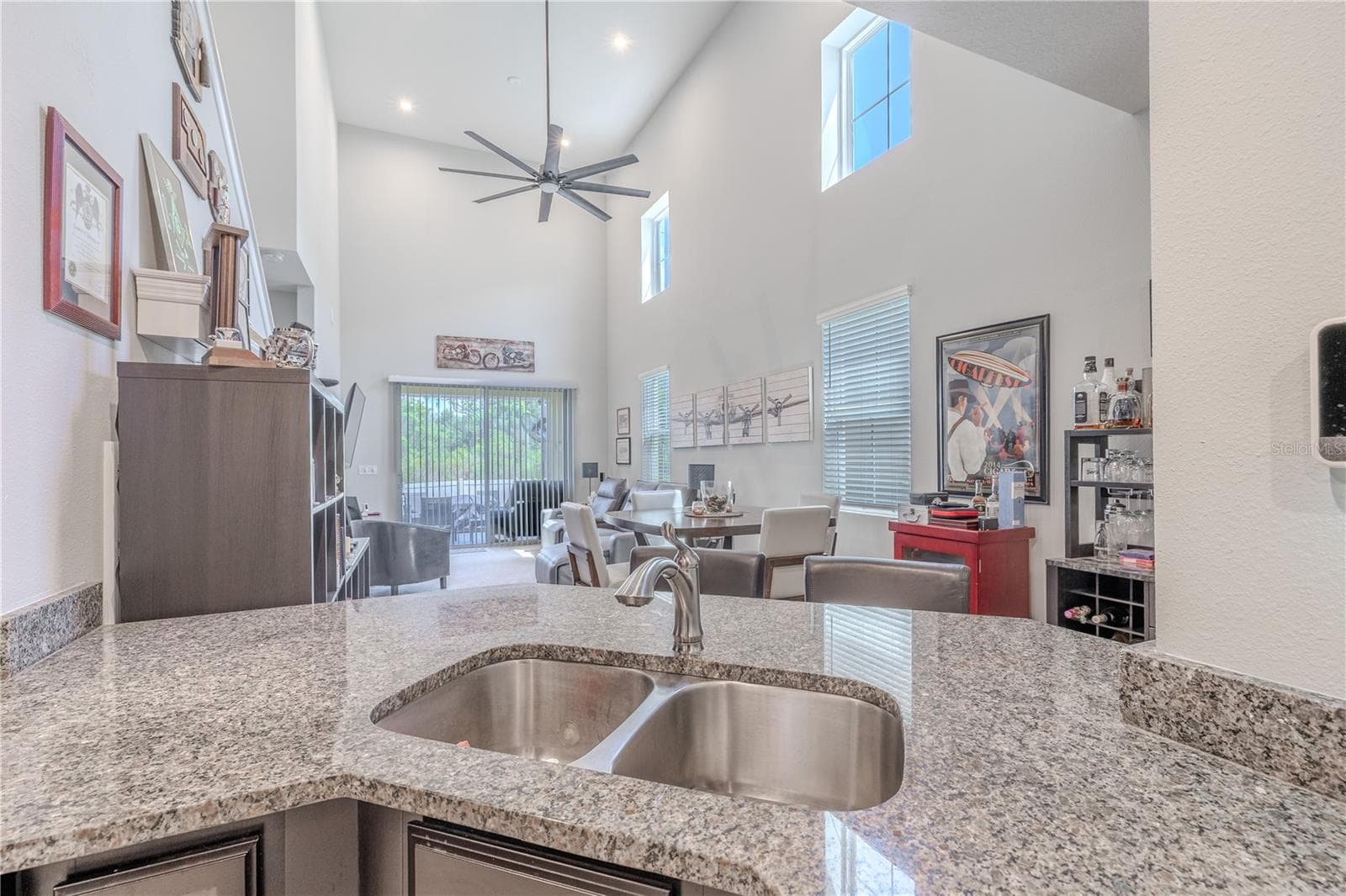 From the kitchen, the open living and dining area feels especially spacious beneath a soaring vaulted ceiling, with high-set windows adding natural light and sliding glass doors extending the view toward the screened lanai and greenery beyond. - 3029 JACOB CROSSING LN, HOLIDAY