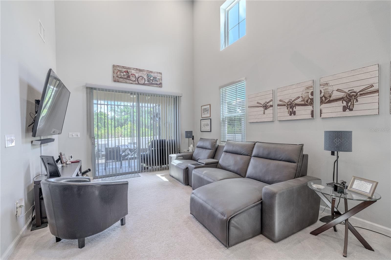 The living room offers plenty of space for comfortable seating beneath the soaring ceiling, with a tall window and sliding glass doors bringing in natural light and opening to the screened lanai. - 3029 JACOB CROSSING LN, HOLIDAY