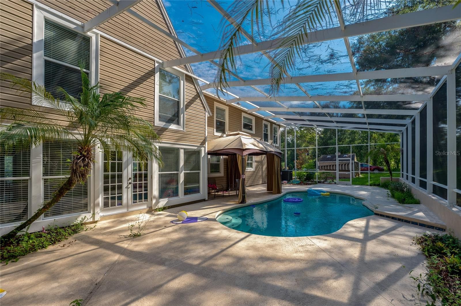 Sunlit outdoor pool deck enclosed in a screened lanai, highlighting French doors leading inside and lush tropical landscaping. - 2081 PENNSYLVANIA DR, DELAND