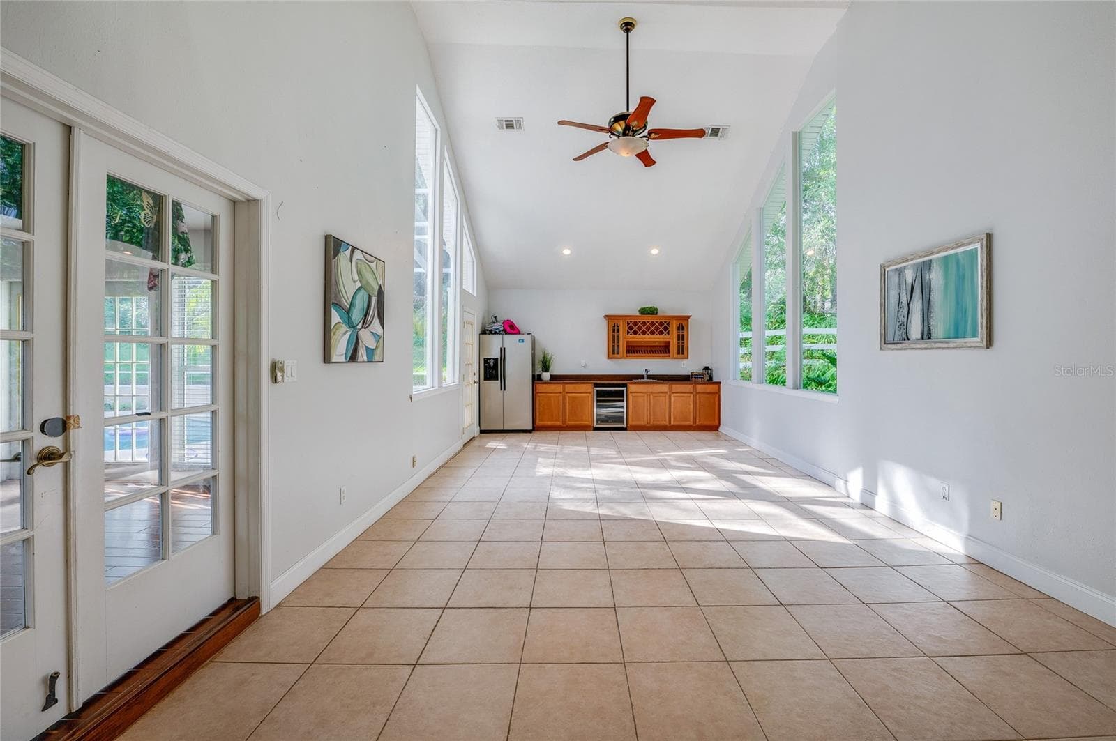 Spacious sunlit flex room featuring vaulted ceilings, a ceiling fan, wall-to-wall tile flooring, and floor-to-ceiling windows overlooking lush greenery. - 2081 PENNSYLVANIA DR, DELAND
