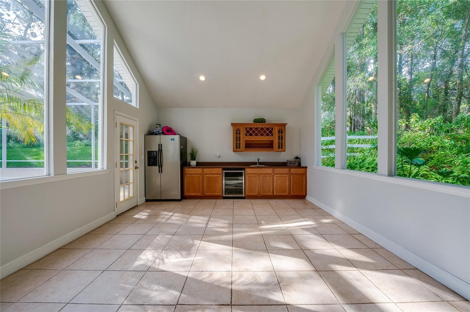 Flex space filled with natural light from floor-to-ceiling windows, featuring tiled floors, vaulted ceilings, and a built-in wet bar setup. - 2081 PENNSYLVANIA DR, DELAND