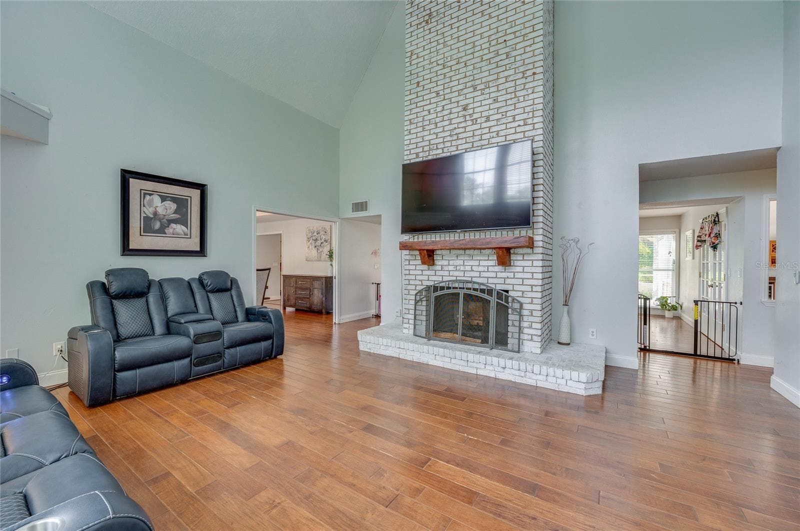 Soaring living room view centered around a floor-to-ceiling whitewashed brick fireplace with a rustic mantel and laminate flooring throughout. - 2081 PENNSYLVANIA DR, DELAND