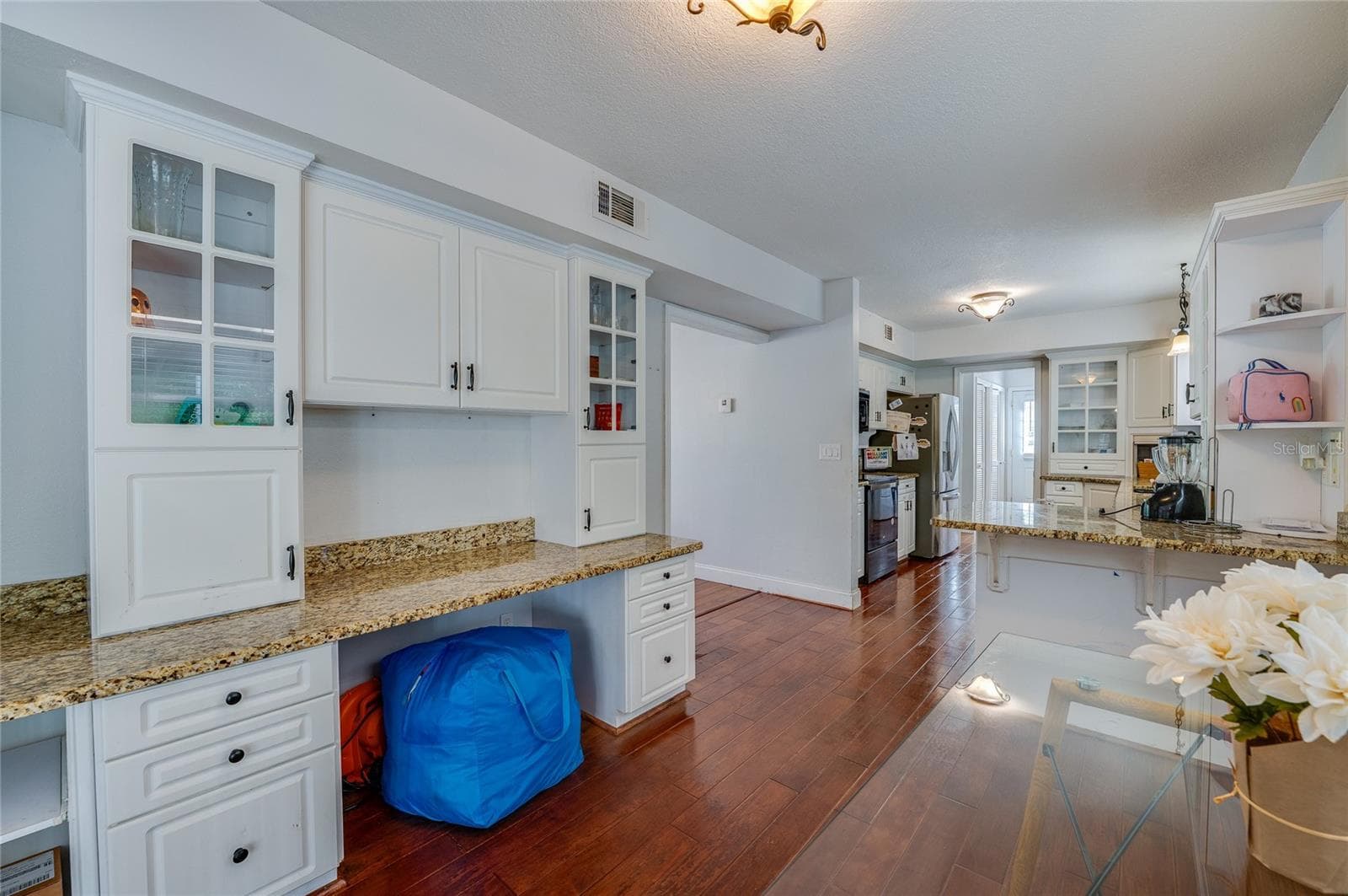 Bright kitchen prep space featuring white cabinetry with glass-front uppers, granite countertops, and seamless laminate flooring leading to adjacent rooms. - 2081 PENNSYLVANIA DR, DELAND