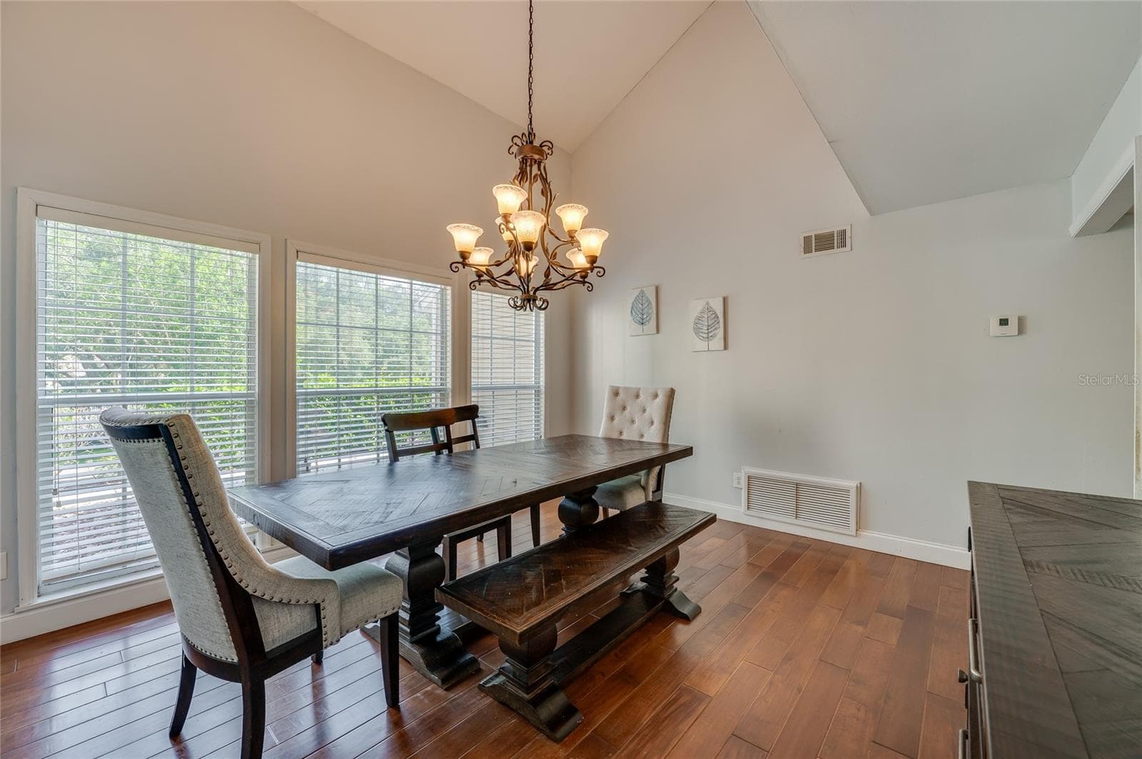 Formal dining area framed by vaulted ceilings and expansive windows, lit by an ornate iron chandelier over rich laminate floors. - 2081 PENNSYLVANIA DR, DELAND
