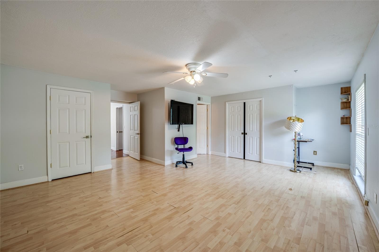 Wide interior shot of a spacious room with light laminate flooring, a ceiling fan, and multiple white panel doors. - 2081 PENNSYLVANIA DR, DELAND