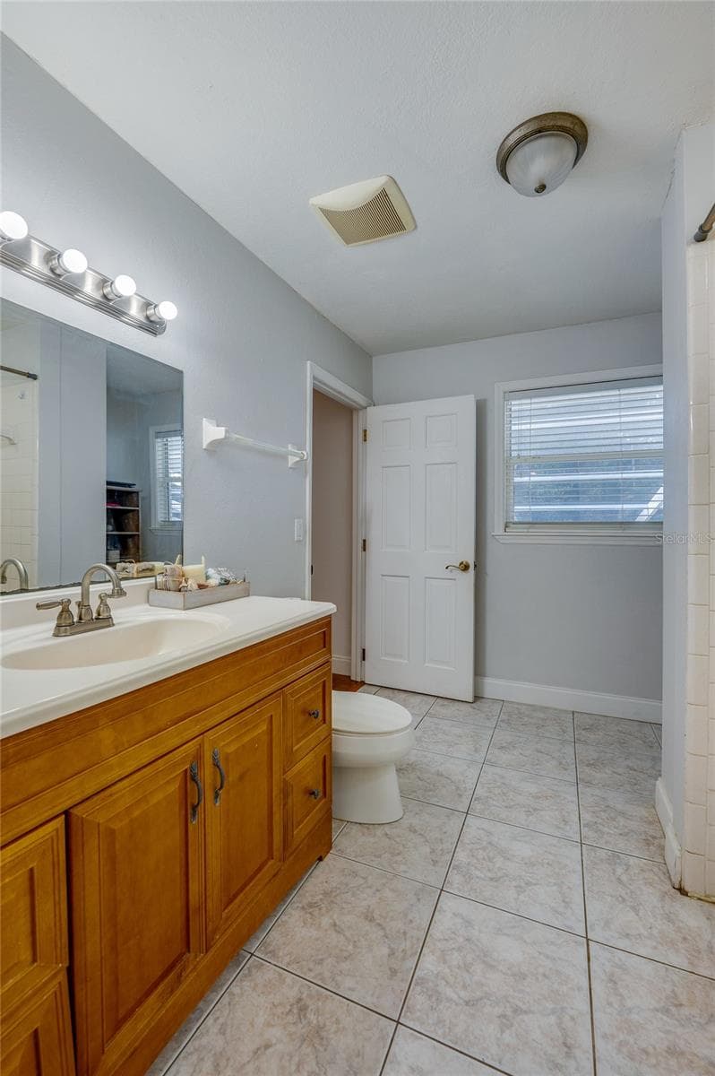 Full bathroom featuring tiled flooring, a warm wood vanity with a large mirror, and light blue walls. - 2081 PENNSYLVANIA DR, DELAND