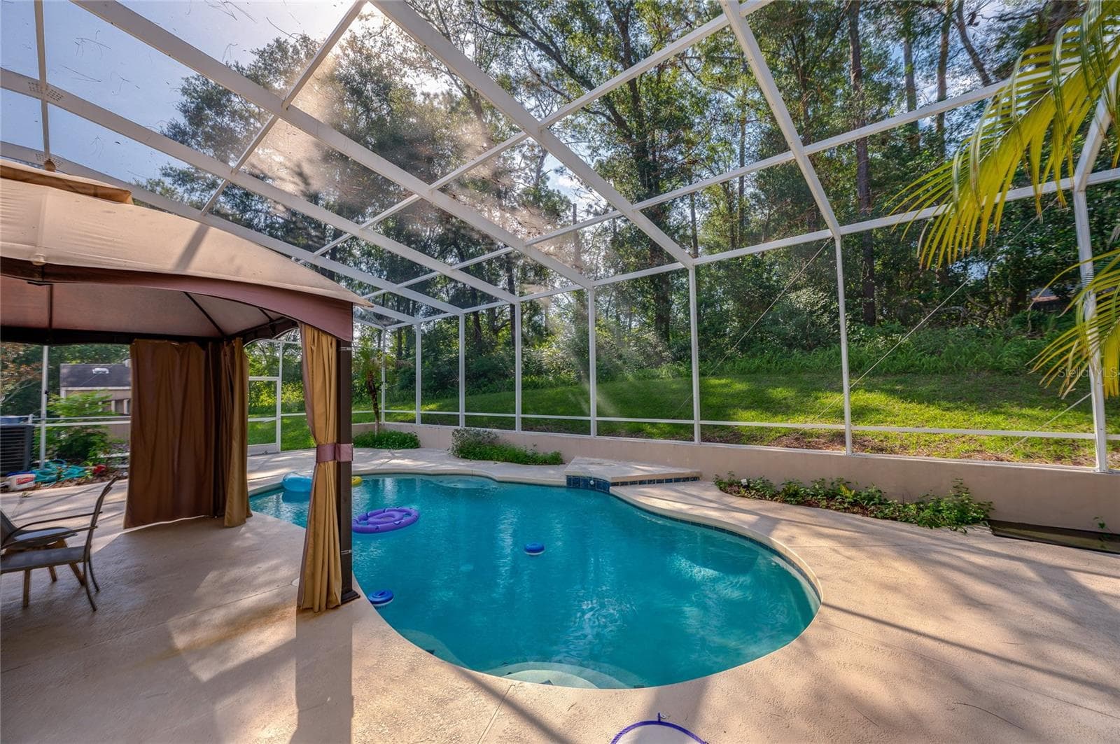 Screened-in patio enclosure sheltering a private in-ground swimming pool surrounded by a spacious concrete deck and mature trees. - 2081 PENNSYLVANIA DR, DELAND