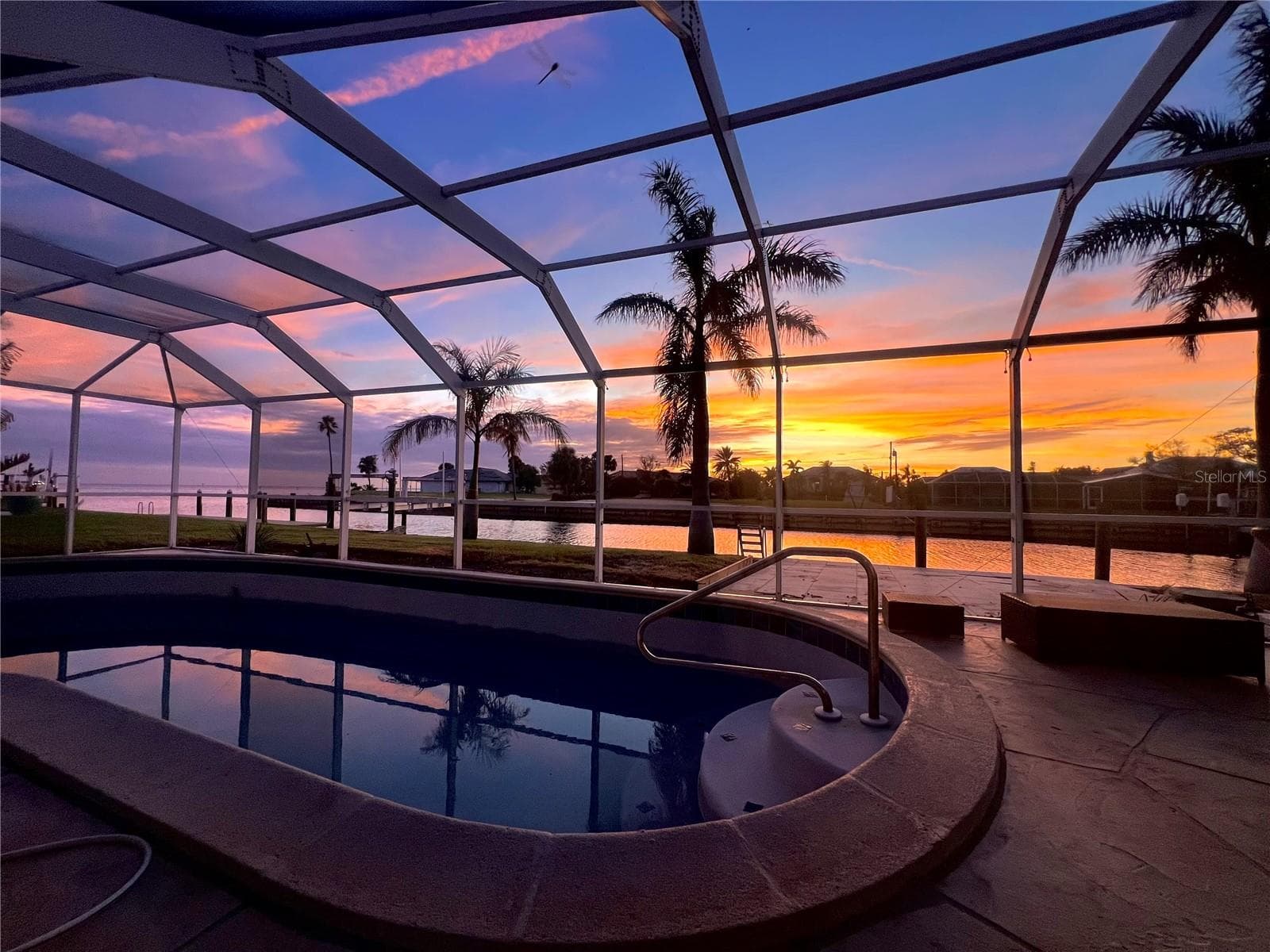 Pool at Sunset – Beautiful evening view from the screened pool area showcasing a colorful Southwest Florida sunset over the waterfront. - 4449 CREWS CT, PORT CHARLOTTE