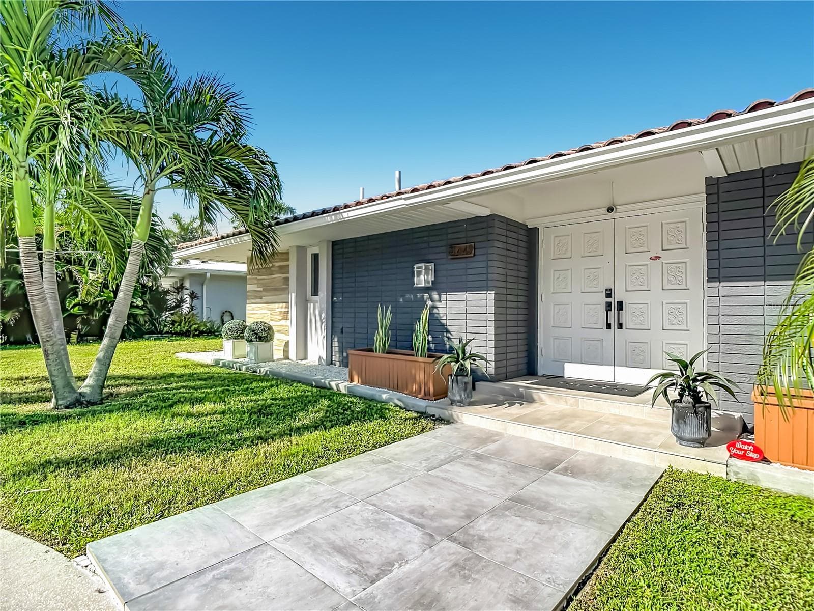 Front Exterior – Welcoming front exterior featuring a contemporary entrance, attached garage, mature palm trees, and landscaped front yard. - 4449 CREWS CT, PORT CHARLOTTE