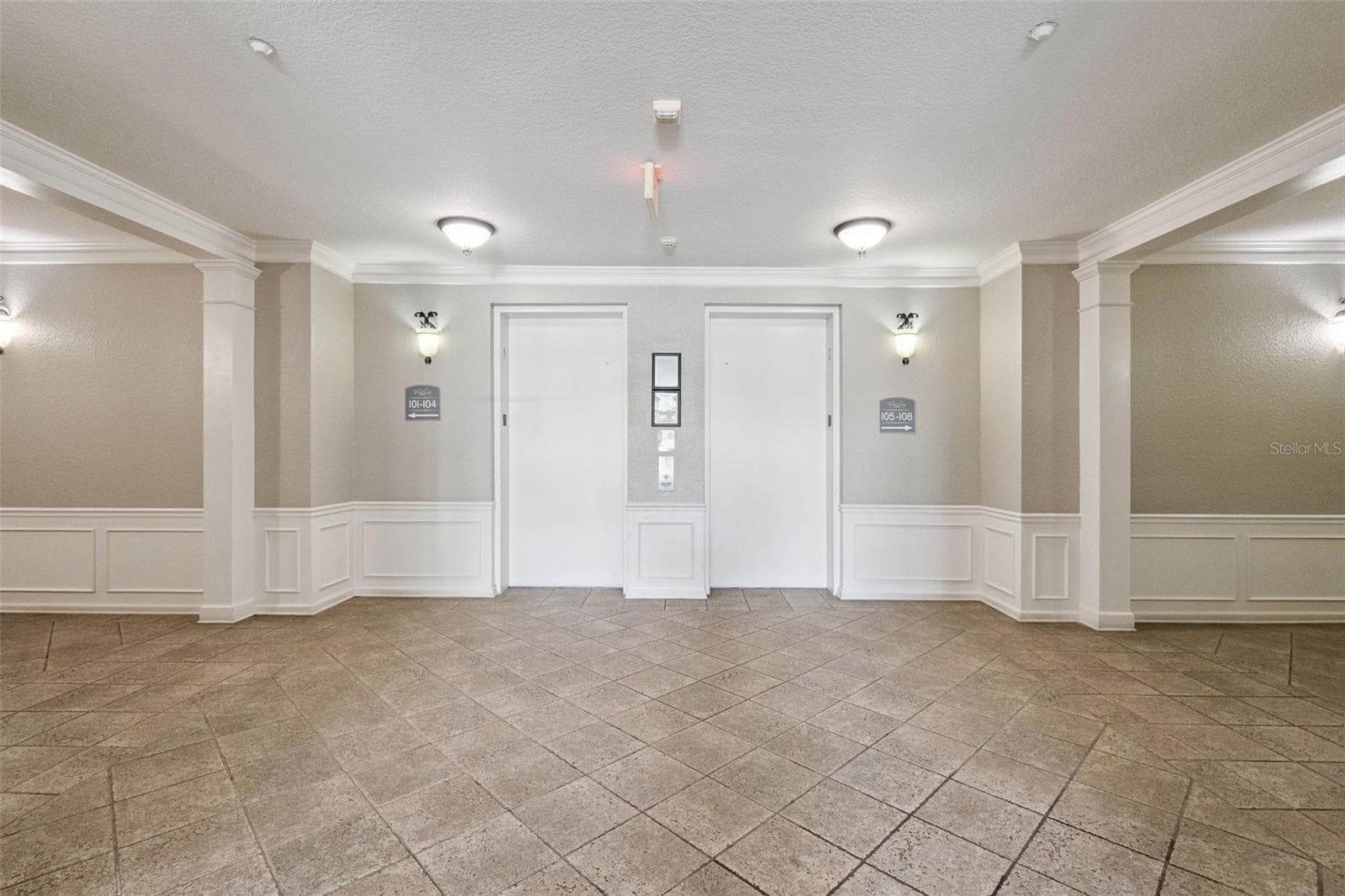 Elevator Lobby:Spacious interior building lobby featuring tiled flooring, classic wainscoting, warm wall sconces, and dual elevator access. - 4840 CAYVIEW AVE #405, ORLANDO