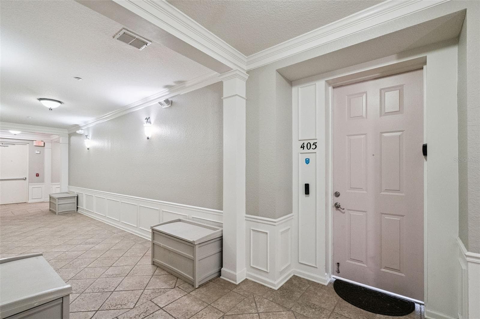 Interior Hallway:Well-lit interior corridor showcasing tiled flooring, wainscoting trim, storage benches, and private entrance to Unit 405. - 4840 CAYVIEW AVE #405, ORLANDO