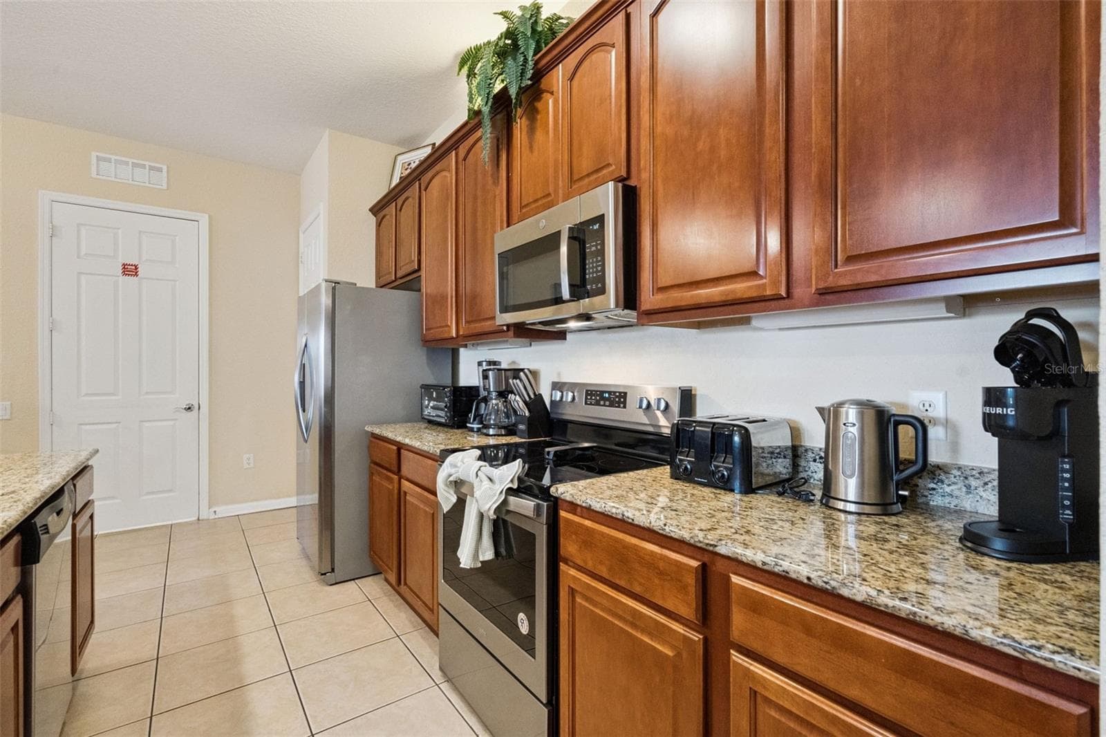 Kitchen Prep & Storage Area:Functional counter space highlighting rich wood upper and lower cabinets, granite counters, glass-top range, built-in microwave, and tile flooring. - 4840 CAYVIEW AVE #405, ORLANDO