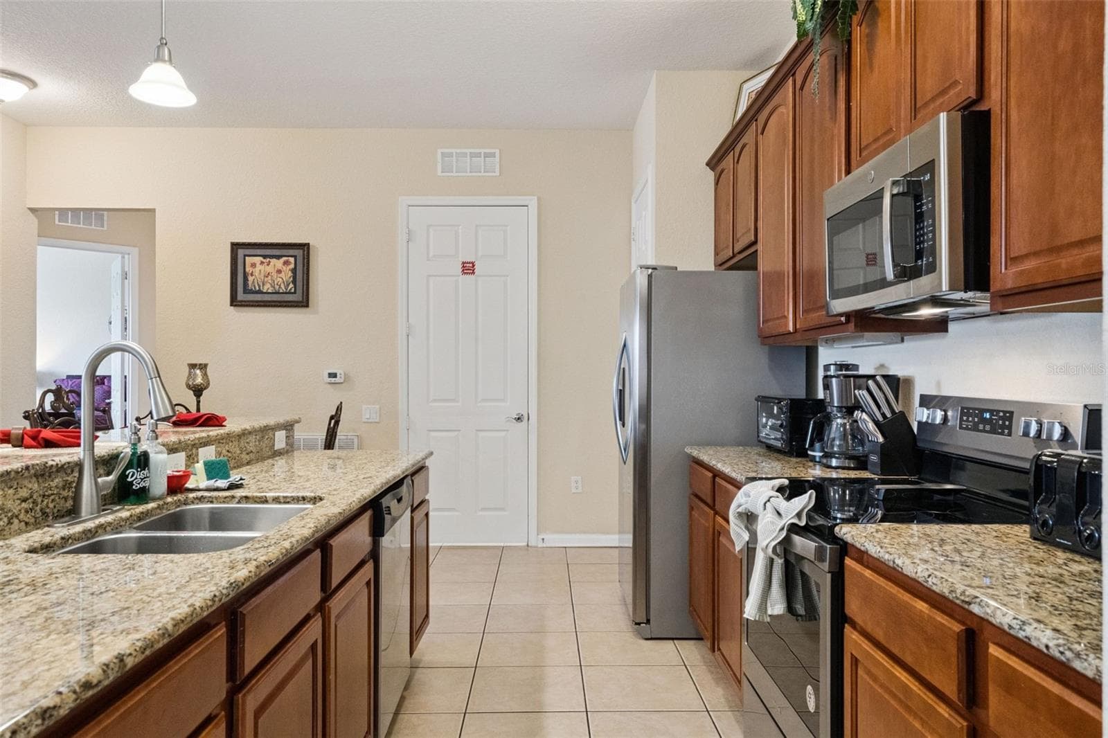Kitchen Corridor:Bright, open kitchen featuring granite countertops, double-basin stainless steel sink, warm wood cabinetry, stainless steel appliances, and low-maintenance tile flooring. - 4840 CAYVIEW AVE #405, ORLANDO
