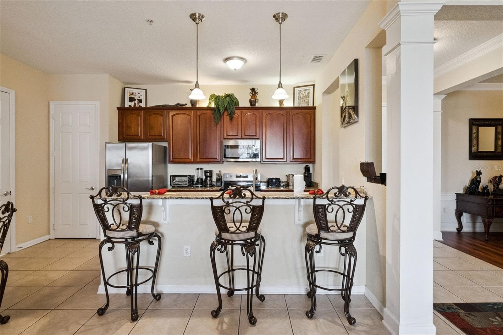 Open Kitchen & Bar Area:Spacious view of the kitchen's raised breakfast bar, showcasing architectural pillar details, tile flooring, and seamless flow into adjoining living spaces. - 4840 CAYVIEW AVE #405, ORLANDO