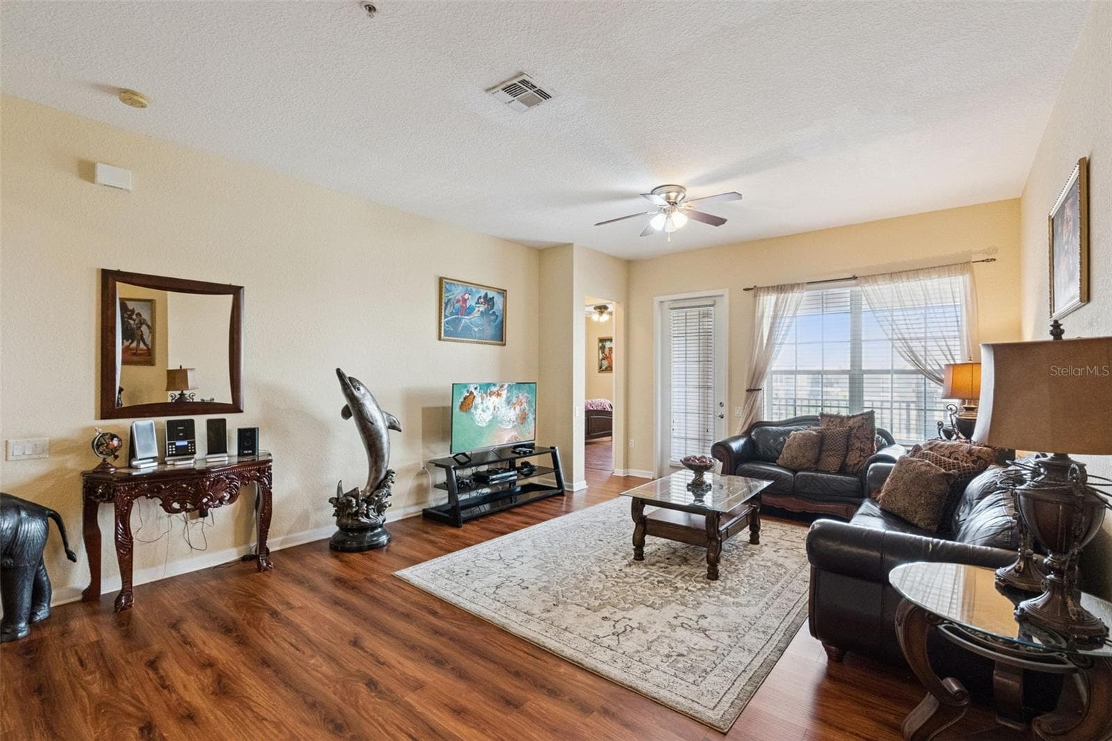 Main Living Room:Bright and spacious living area featuring rich wood-look flooring, ceiling fan, abundant natural light, and direct access to the covered balcony. - 4840 CAYVIEW AVE #405, ORLANDO