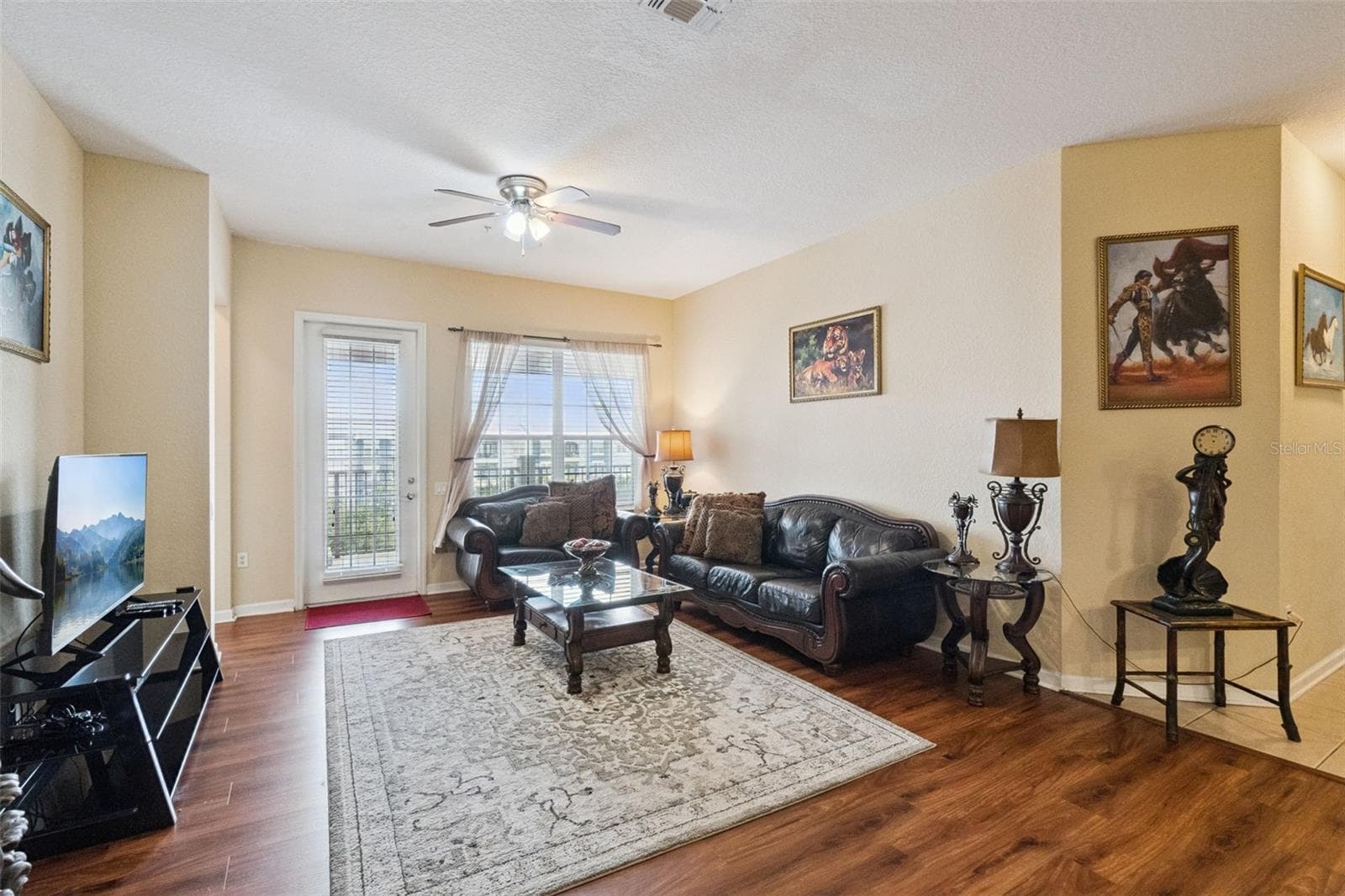 Living Room Layout:Spacious main living room with rich wood-look flooring, ceiling fan, bright windows, and direct access to the covered outdoor balcony. - 4840 CAYVIEW AVE #405, ORLANDO