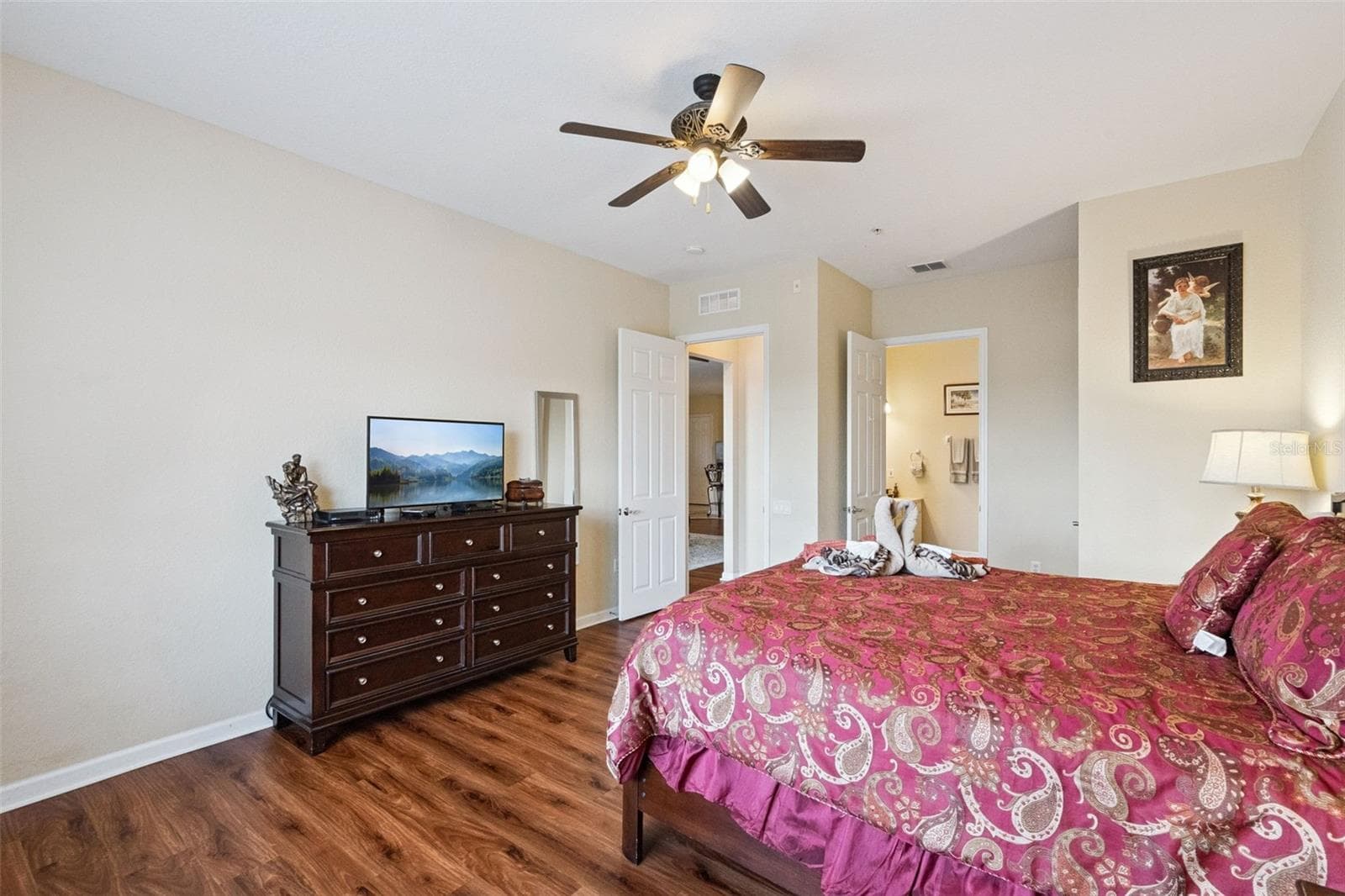 Primary Suite & Bath Entry:Primary bedroom view showing dark wood dresser console, wall-mounted mirror, ceiling fan, and direct doorway access to the private en-suite bathroom. - 4840 CAYVIEW AVE #405, ORLANDO