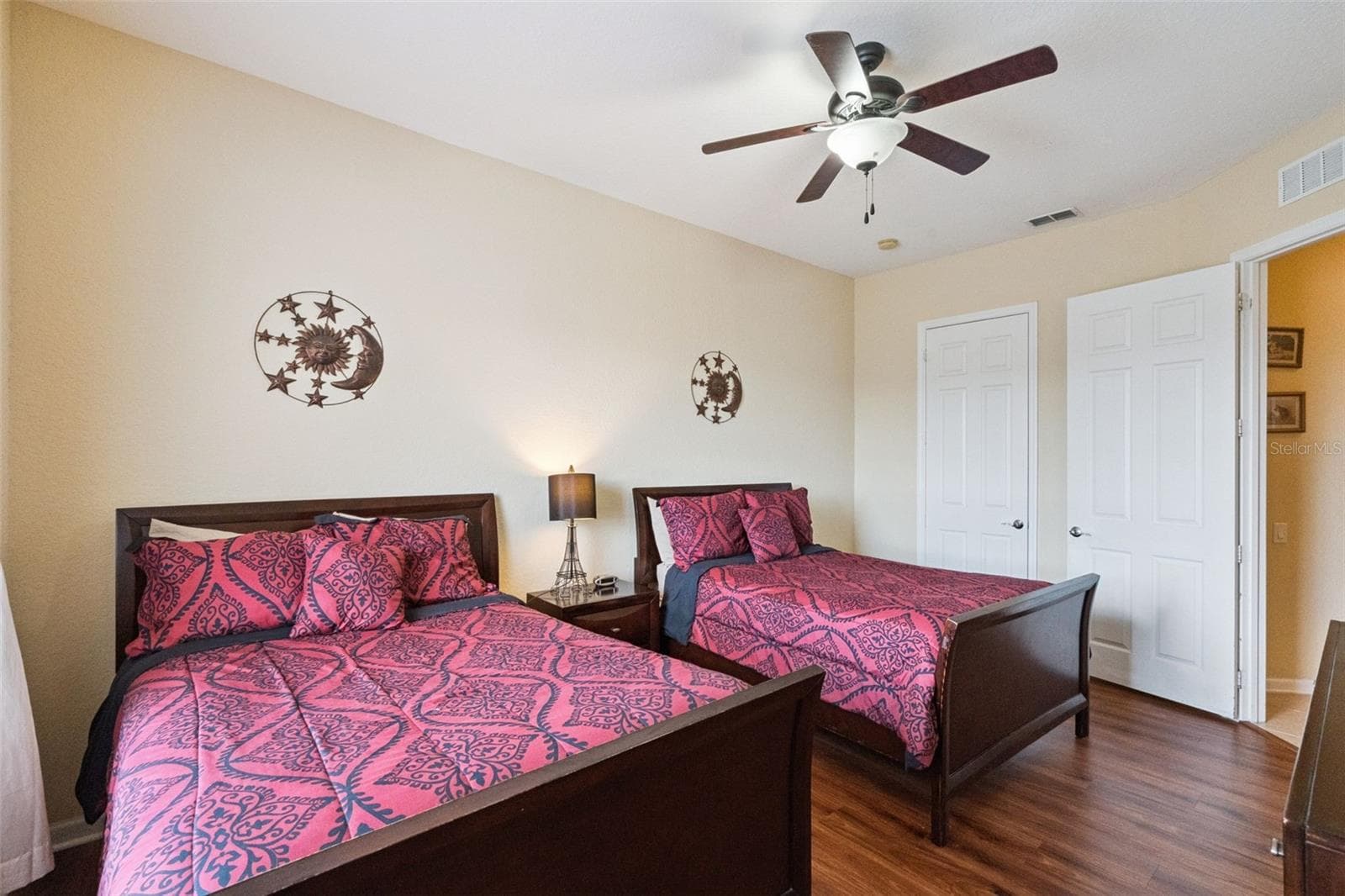 Guest Bedroom Layout:Guest bedroom configured for two full-sized dark wood beds, featuring a central nightstand, white double closet doors, ceiling fan, and durable wood-look flooring. - 4840 CAYVIEW AVE #405, ORLANDO