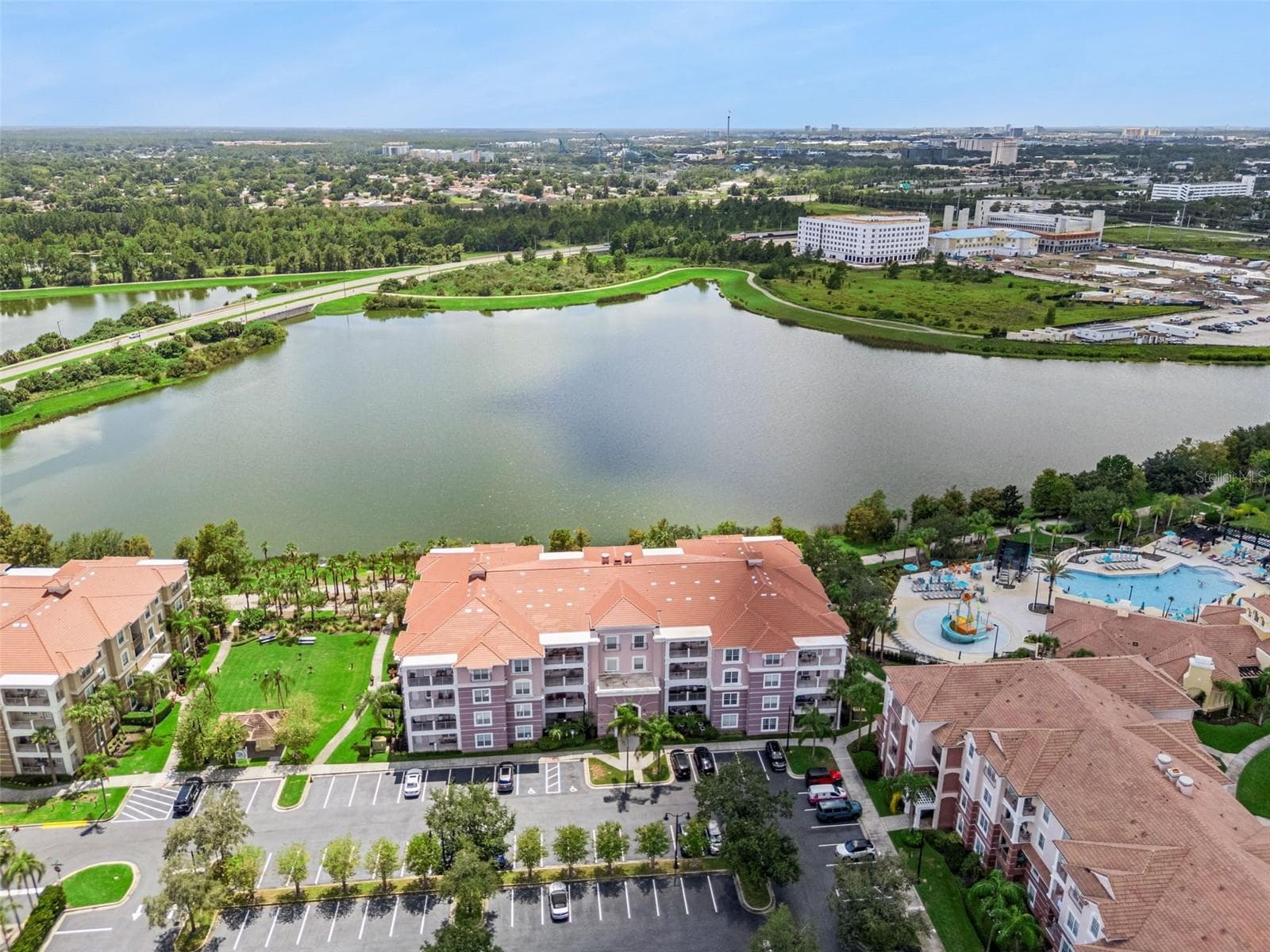 Lake View & Building Front Aerial:Elevated aerial perspective displaying the building facade, ample surface parking, community pool area, and expansive lake backdrop. - 4840 CAYVIEW AVE #405, ORLANDO