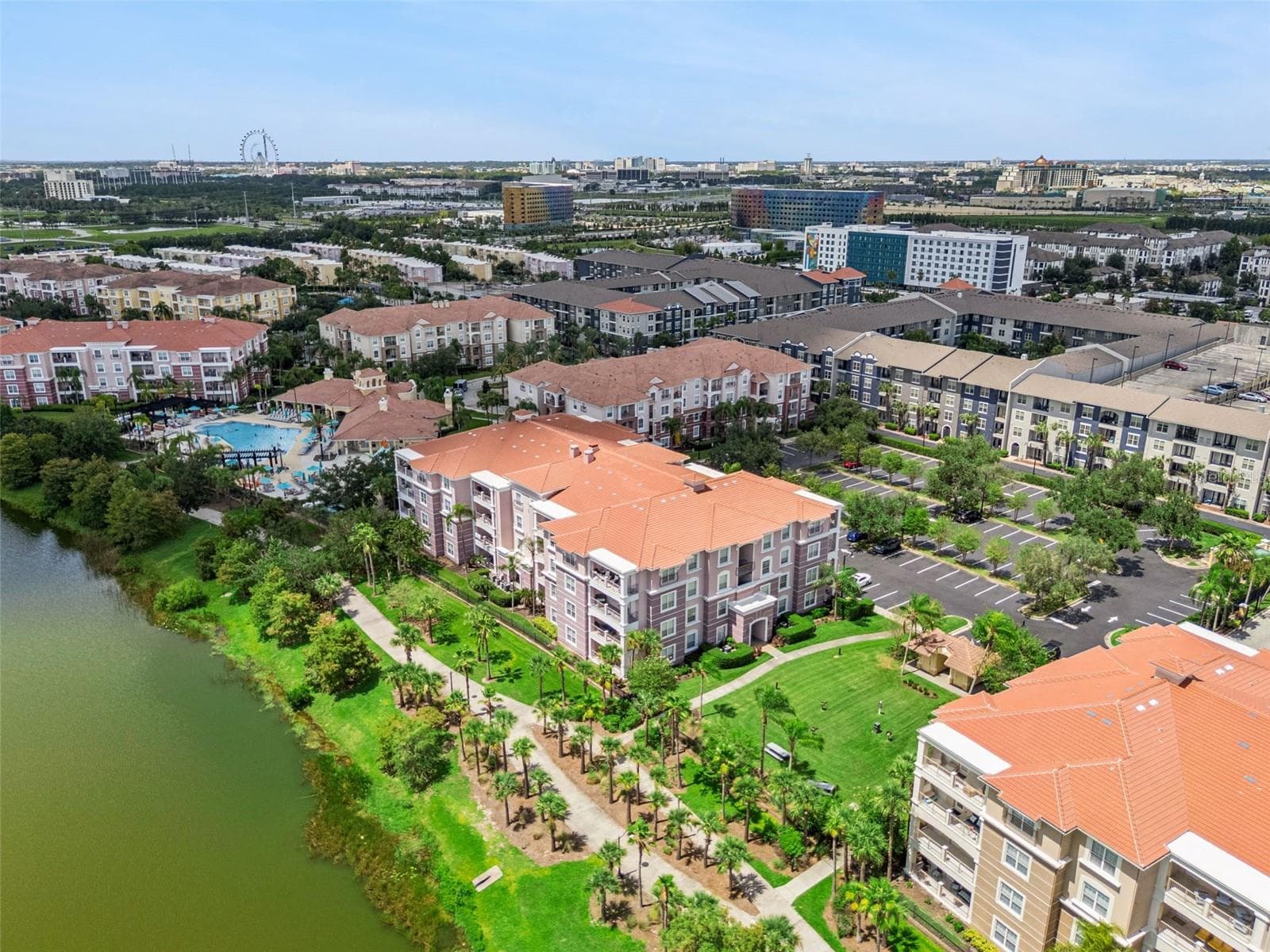 Palm Walk & Lakefront Aerial:High aerial view emphasizing the palm tree-lined walking path, green spaces, waterfront condos, and regional landmark views. - 4840 CAYVIEW AVE #405, ORLANDO
