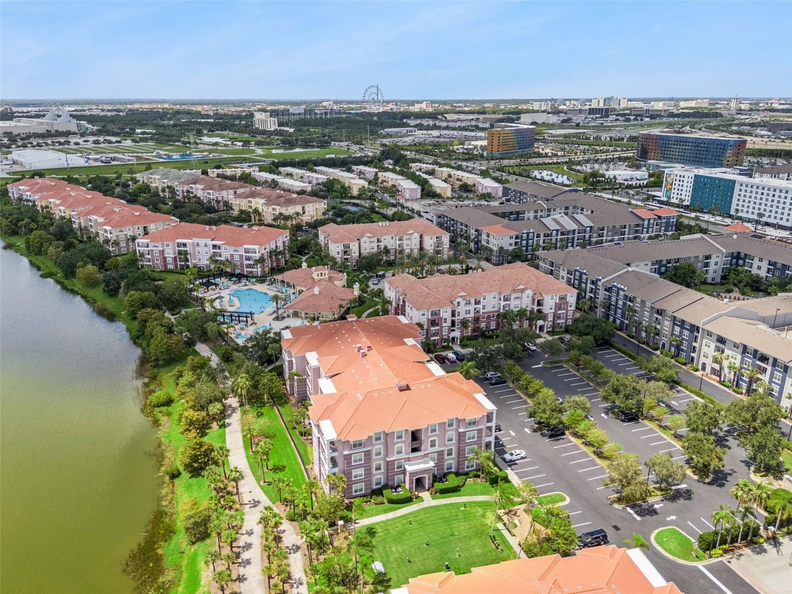 Community Setting Aerial:Broad aerial perspective showcasing the lakefront building placement, green lawn, resort pool, and surrounding cityscape. - 4840 CAYVIEW AVE #405, ORLANDO
