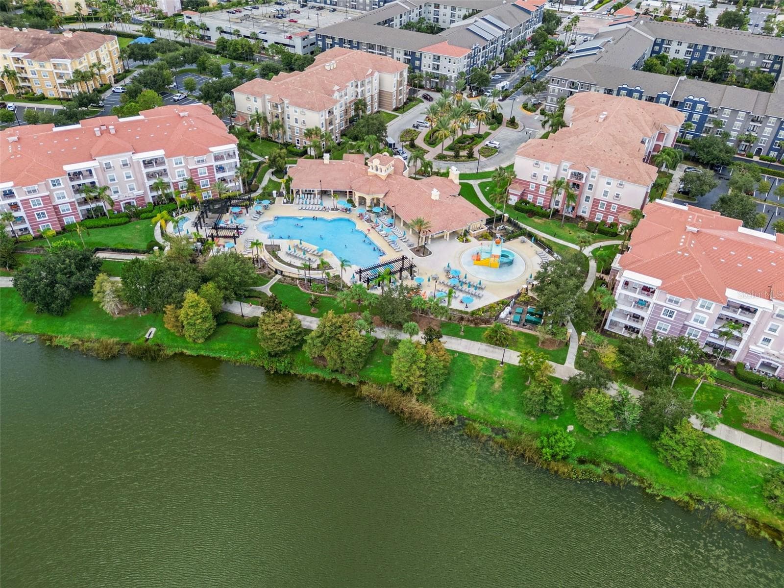 Pool & Clubhouse Aerial:High-angle aerial view highlighting the resort-style pool, kids' splash park, clubhouse amenities, and lakefront walking path. - 4840 CAYVIEW AVE #405, ORLANDO