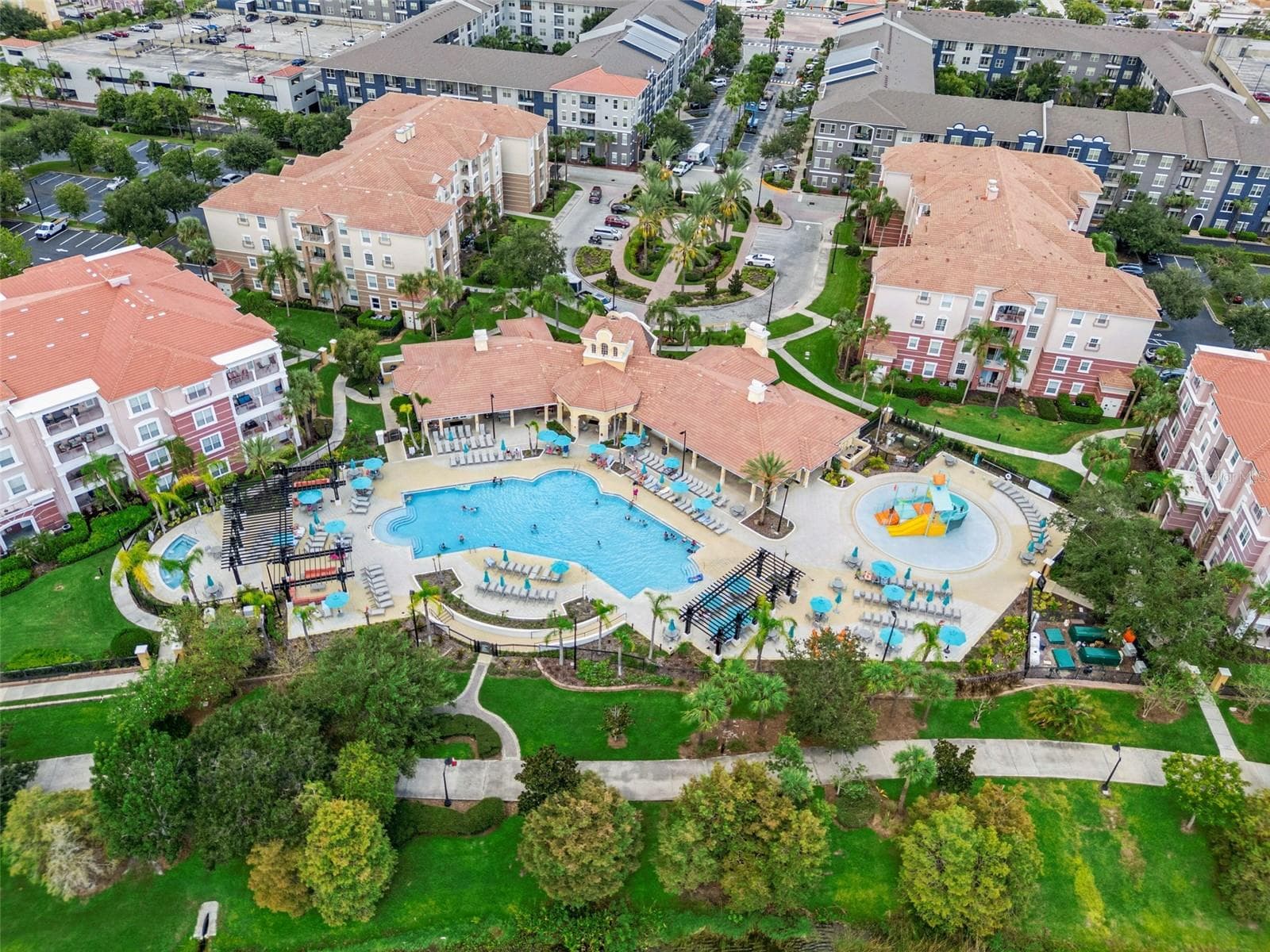 Resort Pool & Amenities Aerial:Aerial birds-eye view highlighting the community's large resort-style pool, children's splash park, expansive sun deck with loungers, clubhouse, and lush tropical landscaping. - 4840 CAYVIEW AVE #405, ORLANDO