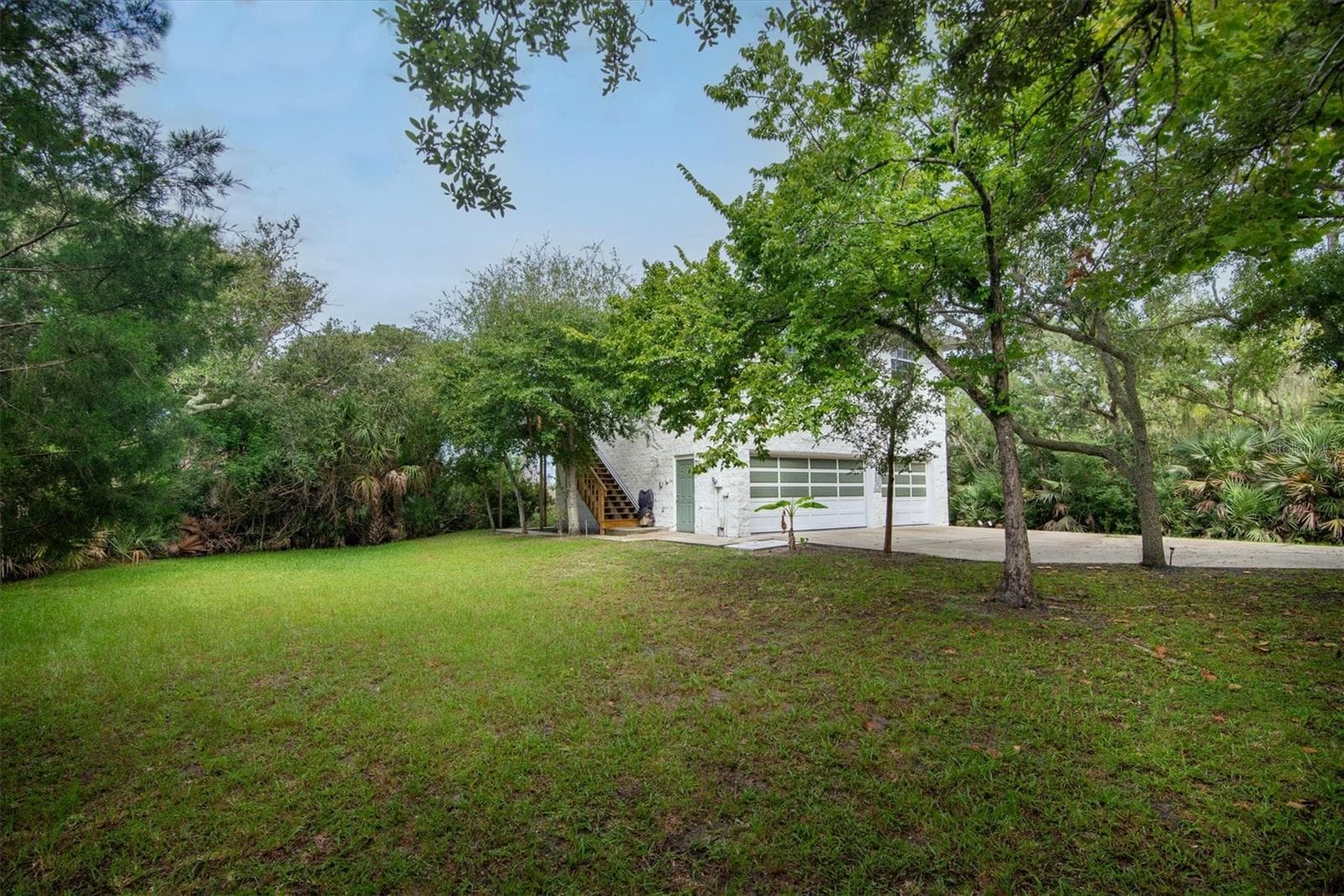 Left side of the property out front with sideview of house showing the garage entry, the stairs and the chairlift to the second floor living area - 1835 OAK PL, FLAGLER BEACH