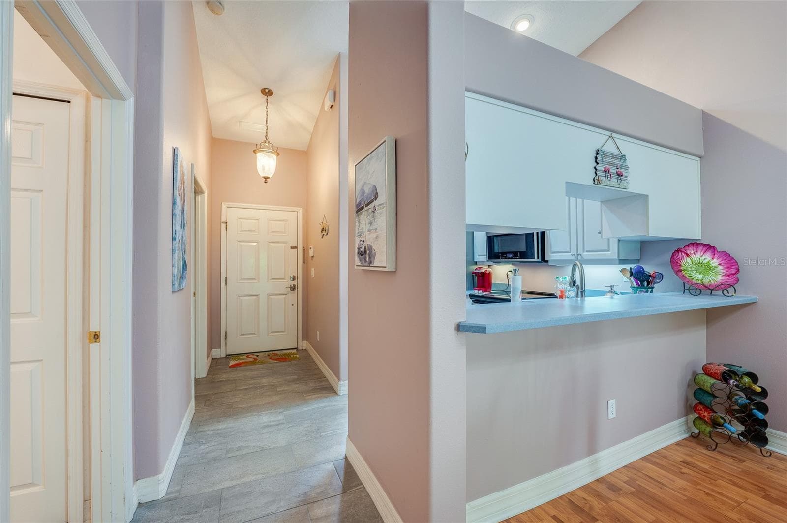 Welcoming home entrance featuring light grey tile flooring, soft purple walls, and a hanging light fixture. A raised breakfast bar overlooks the foyer, creating an open-concept flow. - 1413 COCONUT PALM CIR, PORT ORANGE