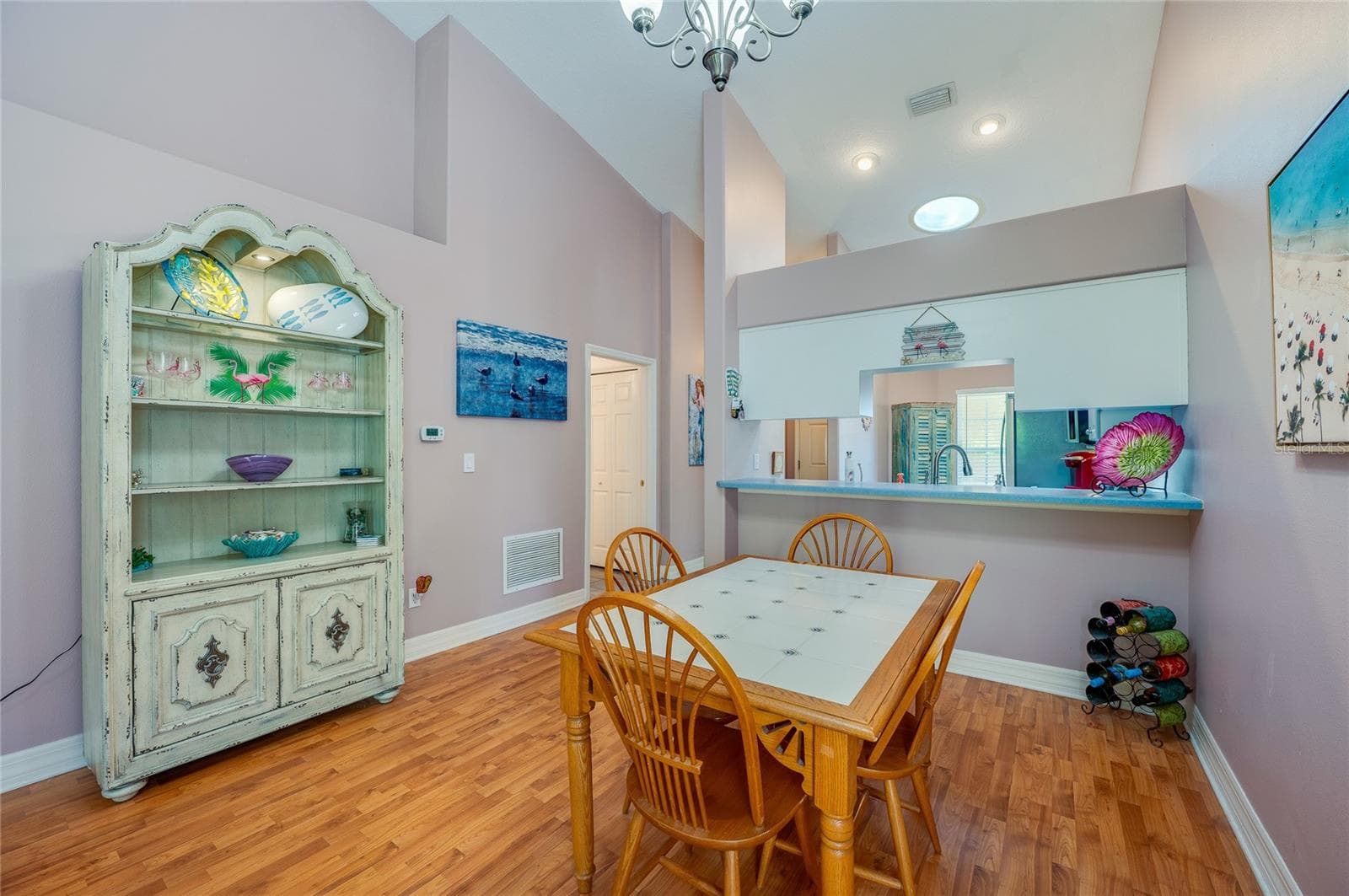 Light-filled dining space featuring high vaulted ceilings, modern overhead lighting, and rich laminate flooring. A low partition wall with a pass-through counter offers a seamless connection directly into the kitchen. - 1413 COCONUT PALM CIR, PORT ORANGE