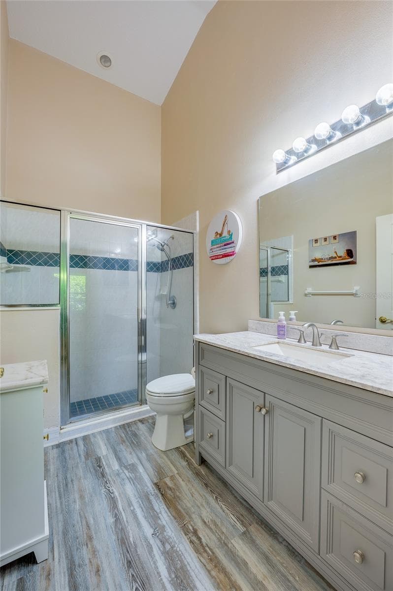 En-suite bathroom featuring a grey vanity with marble counter, modern laminate flooring, and vanity lighting. A glass-enclosed walk-in shower with decorative blue accent tile completes the space. - 1413 COCONUT PALM CIR, PORT ORANGE