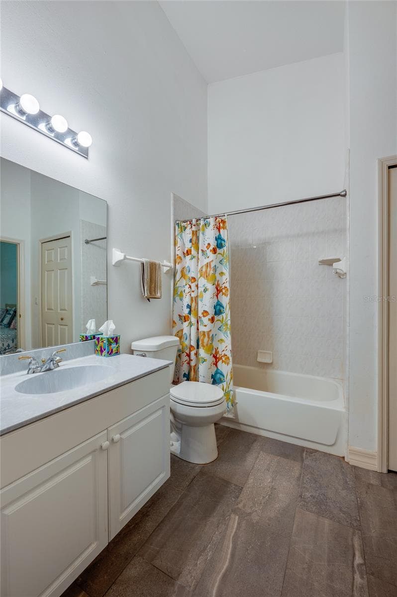 Functional bathroom featuring dark tile flooring, a wide vanity mirror, and bright overhead lighting. The combination shower and bathtub includes built-in wall shelving and tiled surrounds. - 1413 COCONUT PALM CIR, PORT ORANGE