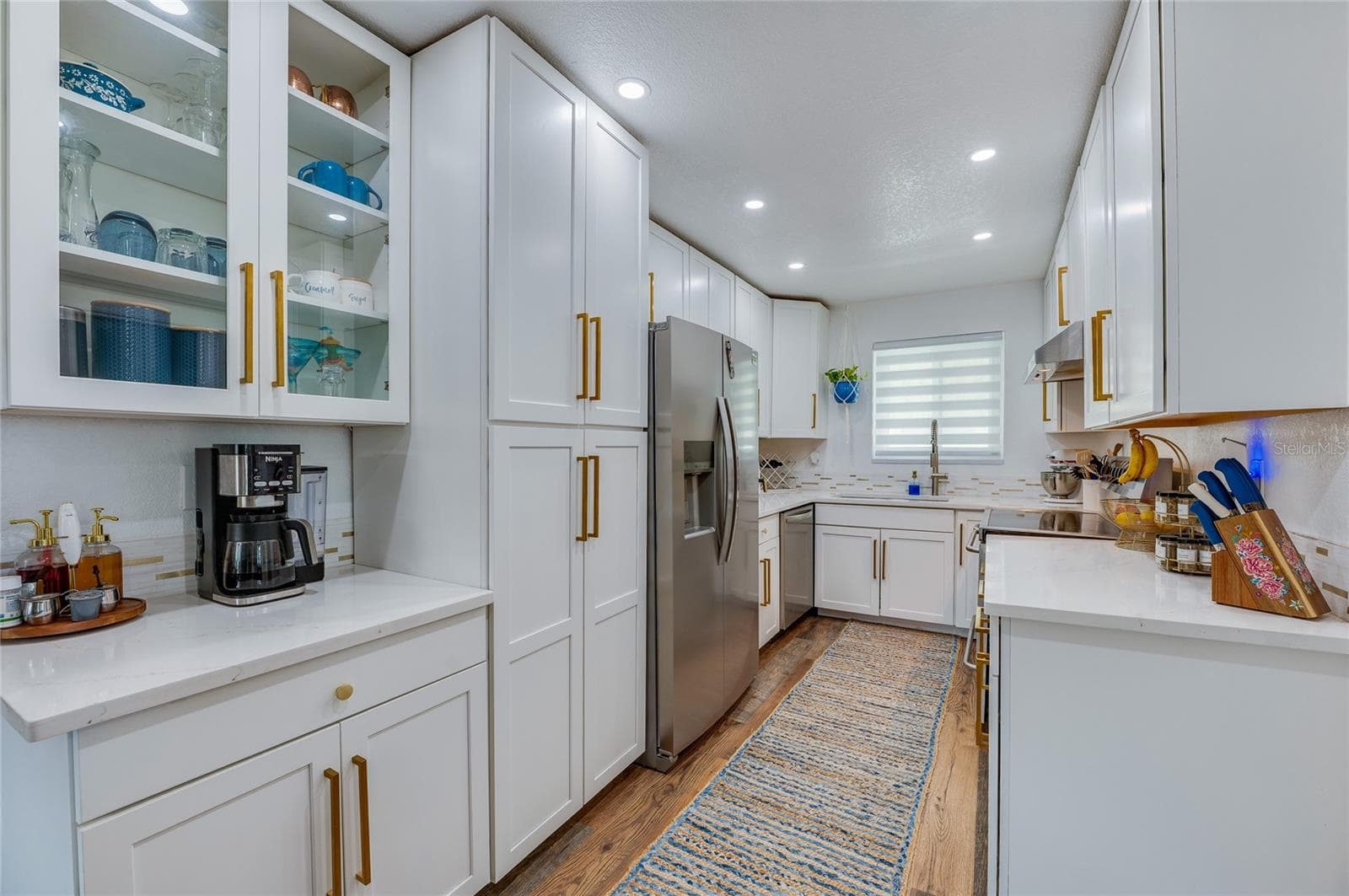 Gourmet galley kitchen featuring crisp white shaker cabinetry, gold hardware accents, stainless steel appliances, and quartz countertops. - 348 WOODLAND AVE, DAYTONA BEACH