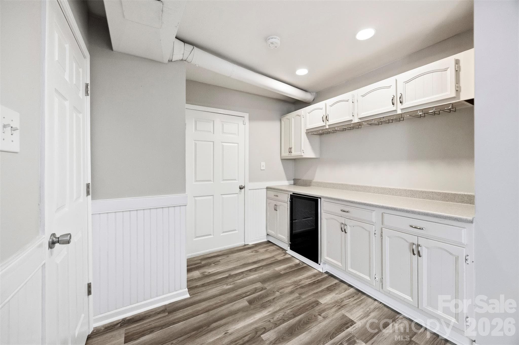 This is a picture of the built in entertainment bar with wine cooler, cabinets and 2 doors. The door in the back of the photo leads to the finished garage. The door to the left of the photo is the stairs going up to the main living spaces. - 6506 Candlewood Drive, Charlotte