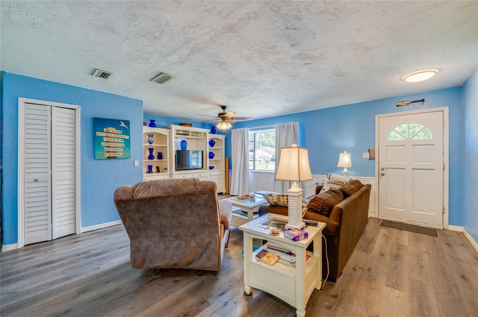 Open living space featuring light blue walls, LVP flooring, double closets, and a white front entry door with glass pane accents. - 146 WESTWOOD DR, DAYTONA BEACH